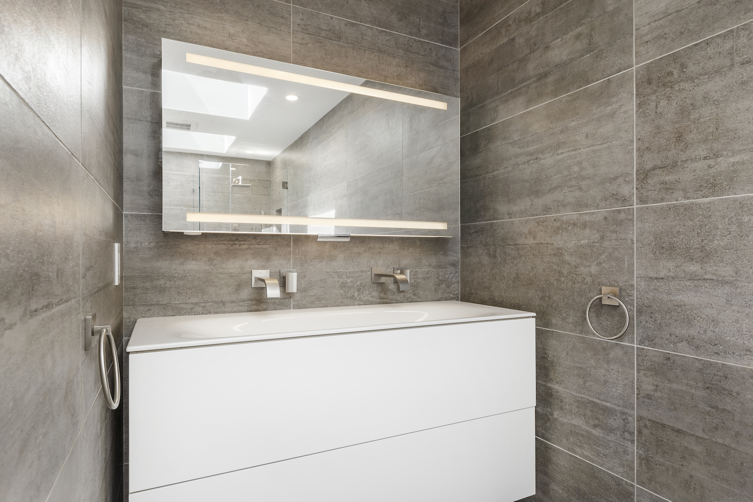 bathroom with grey wall tile and white floating vanity and brushed nickel fixtures.jpg