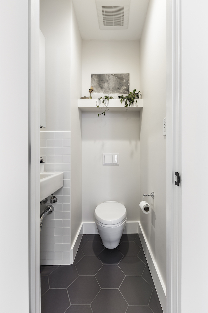 powder room with grey hexagon floor tile and floor mounted toilet and decorative shelving.png