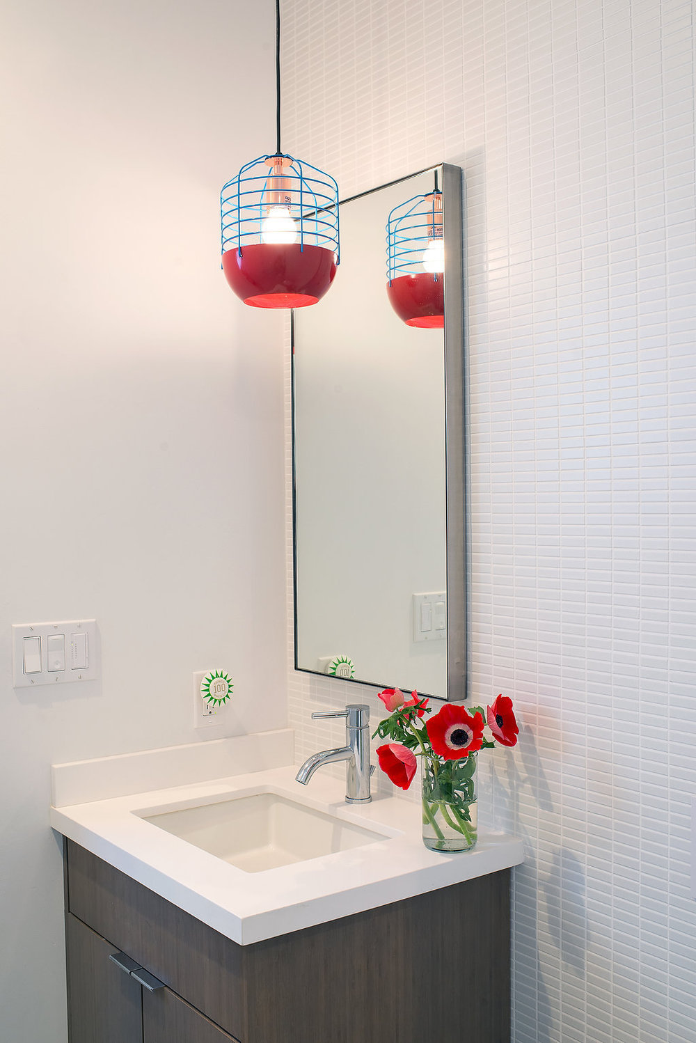 bathroom with wood vanity and white counters and red and blue pendant light and white wall taile and chrome fixtures.jpg