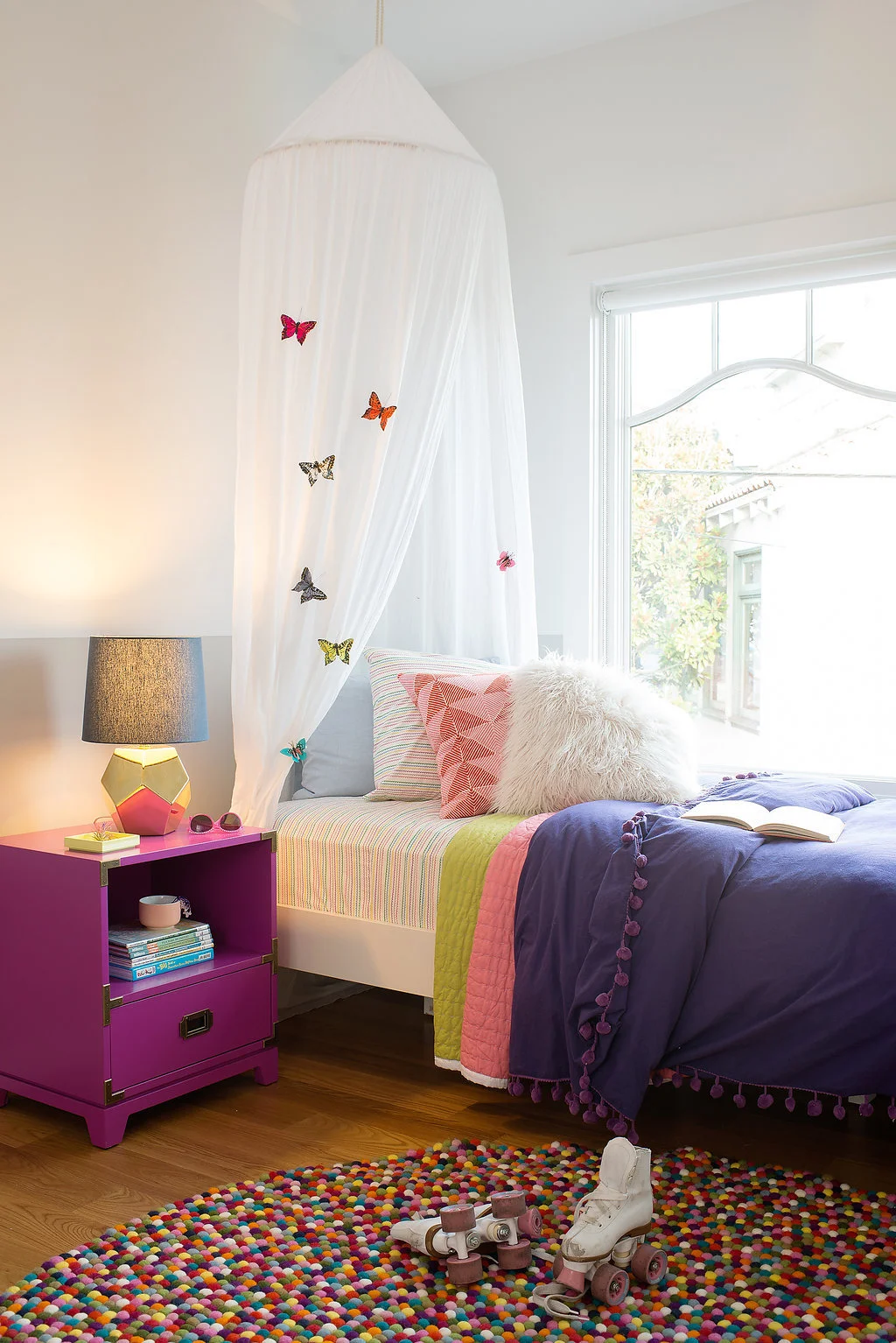 kids bedroom with colorful dotted rug and bed with butterfly canopy and pink nightstand and gold lamp.jpg