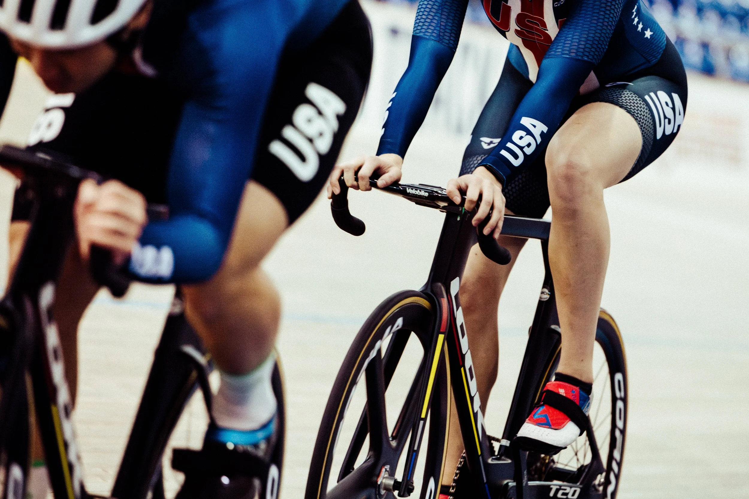 Cyclists racing on a velodrome, dressed in USA team uniforms, riding track bikes.