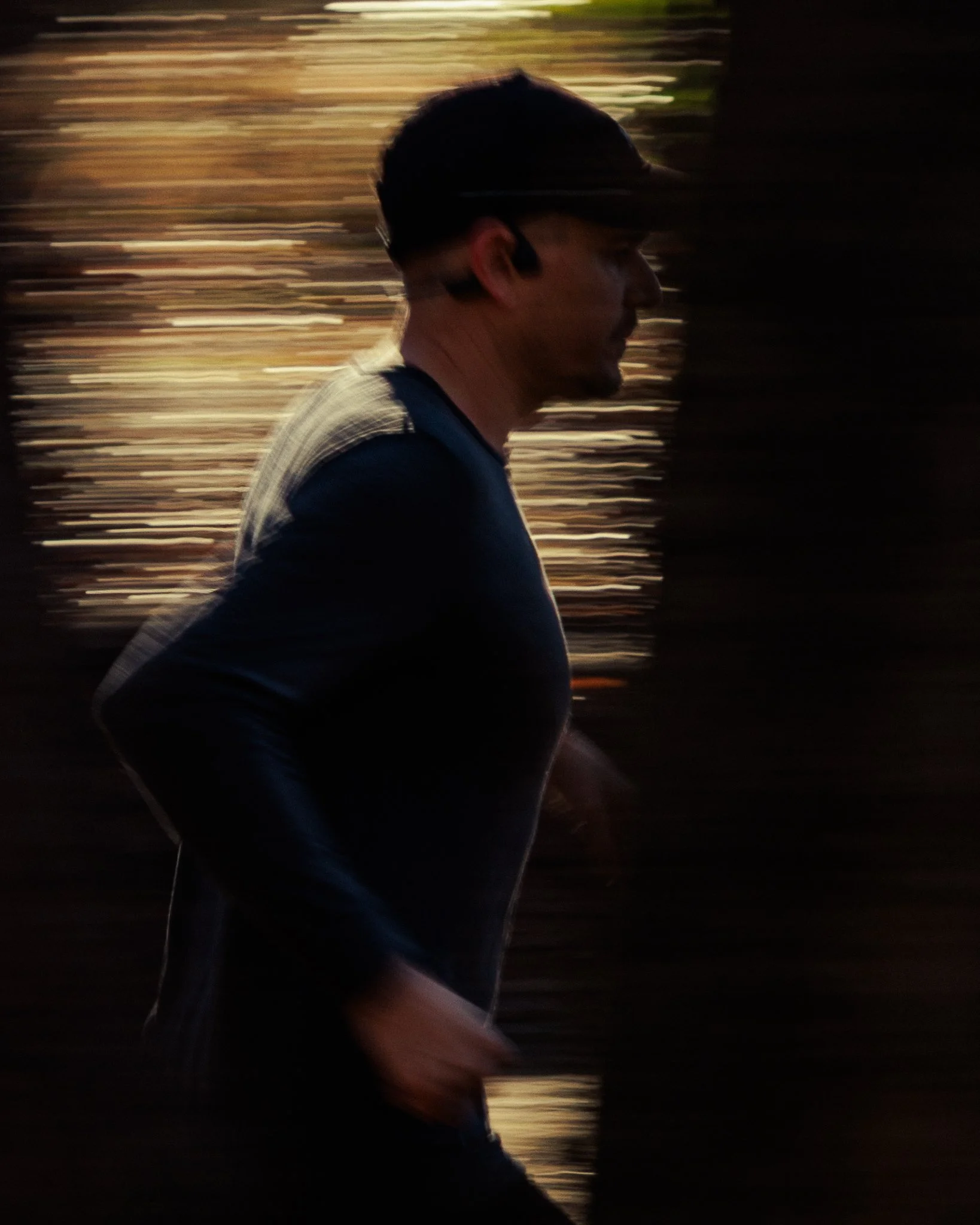 A man running outdoors during sunset or sunrise, with a dark shirt and background of blurred trees and sky.