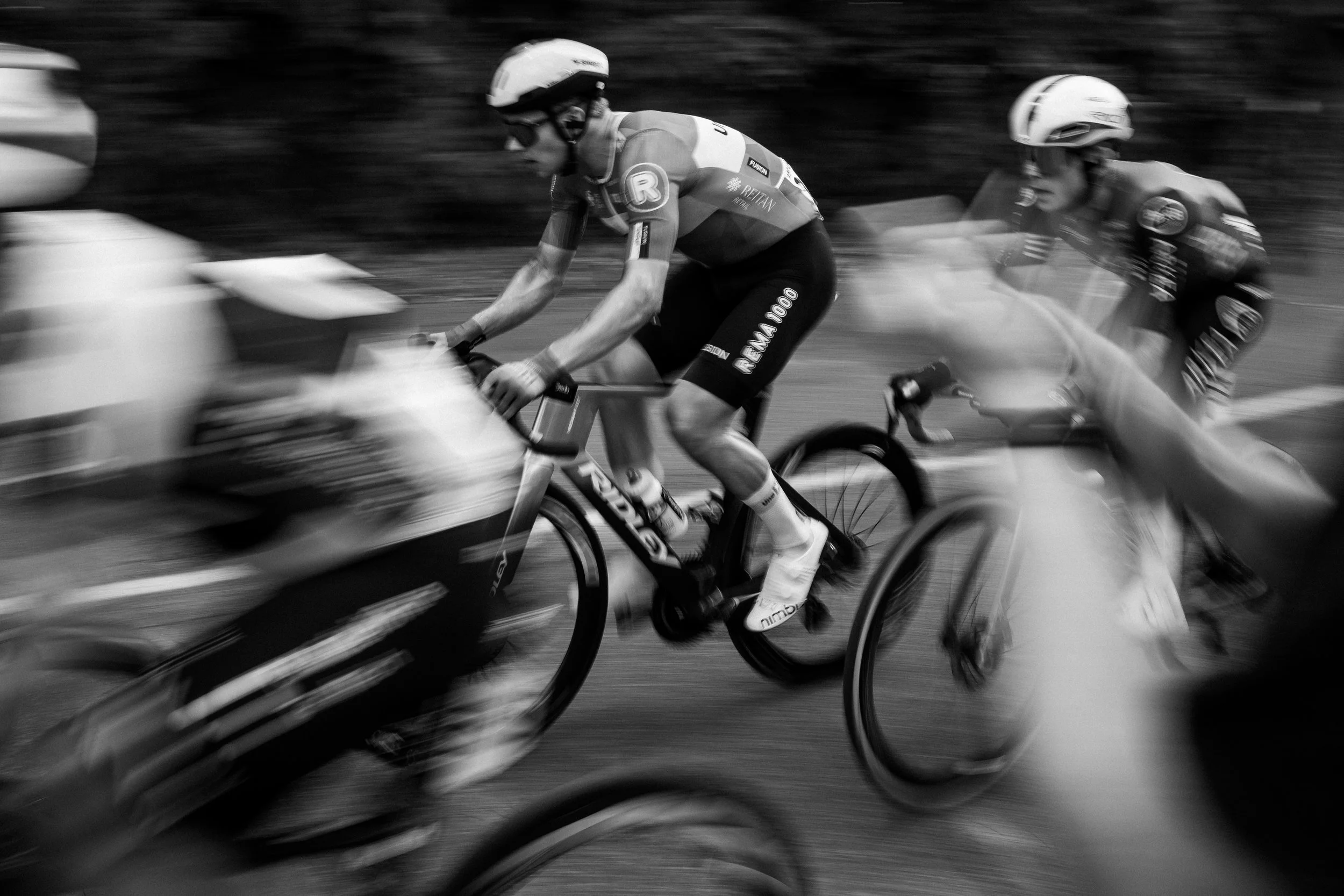 Black and white photo of two cyclists racing, with motion blur highlighting speed.