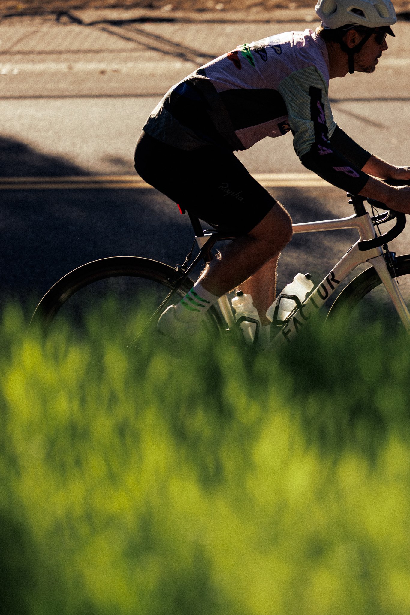 A person riding a white bicycle on a road, wearing a helmet and sunglasses, with sunlight casting shadows.