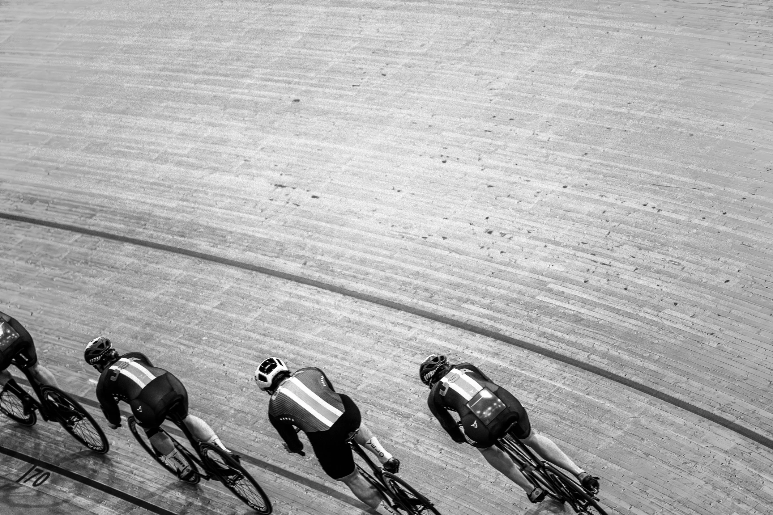 Four cyclists in athletic gear and helmets riding on a wooden velodrome track.