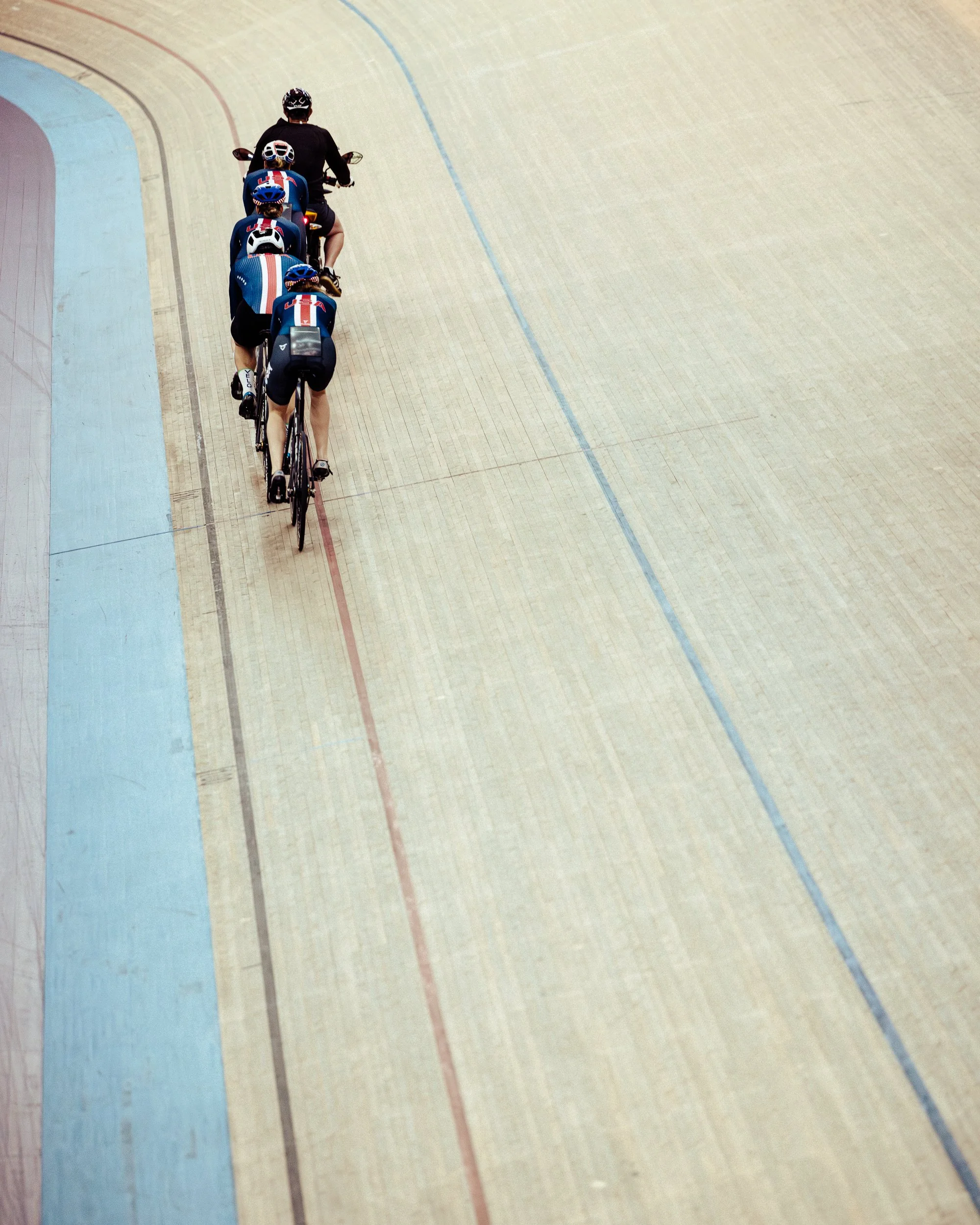 Four cyclists riding on an indoor velodrome track.
