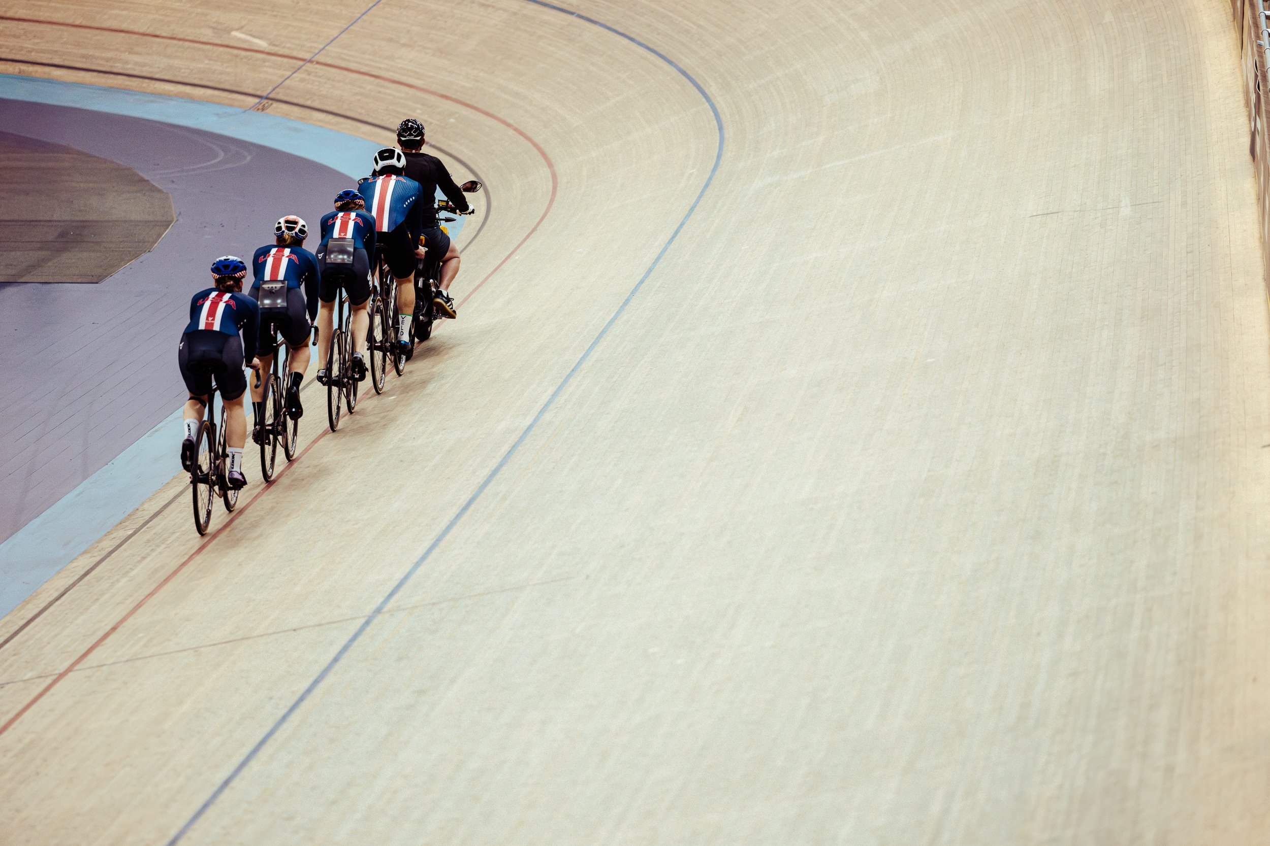 A group of five cyclists in matching uniforms riding on a velodrome track.
