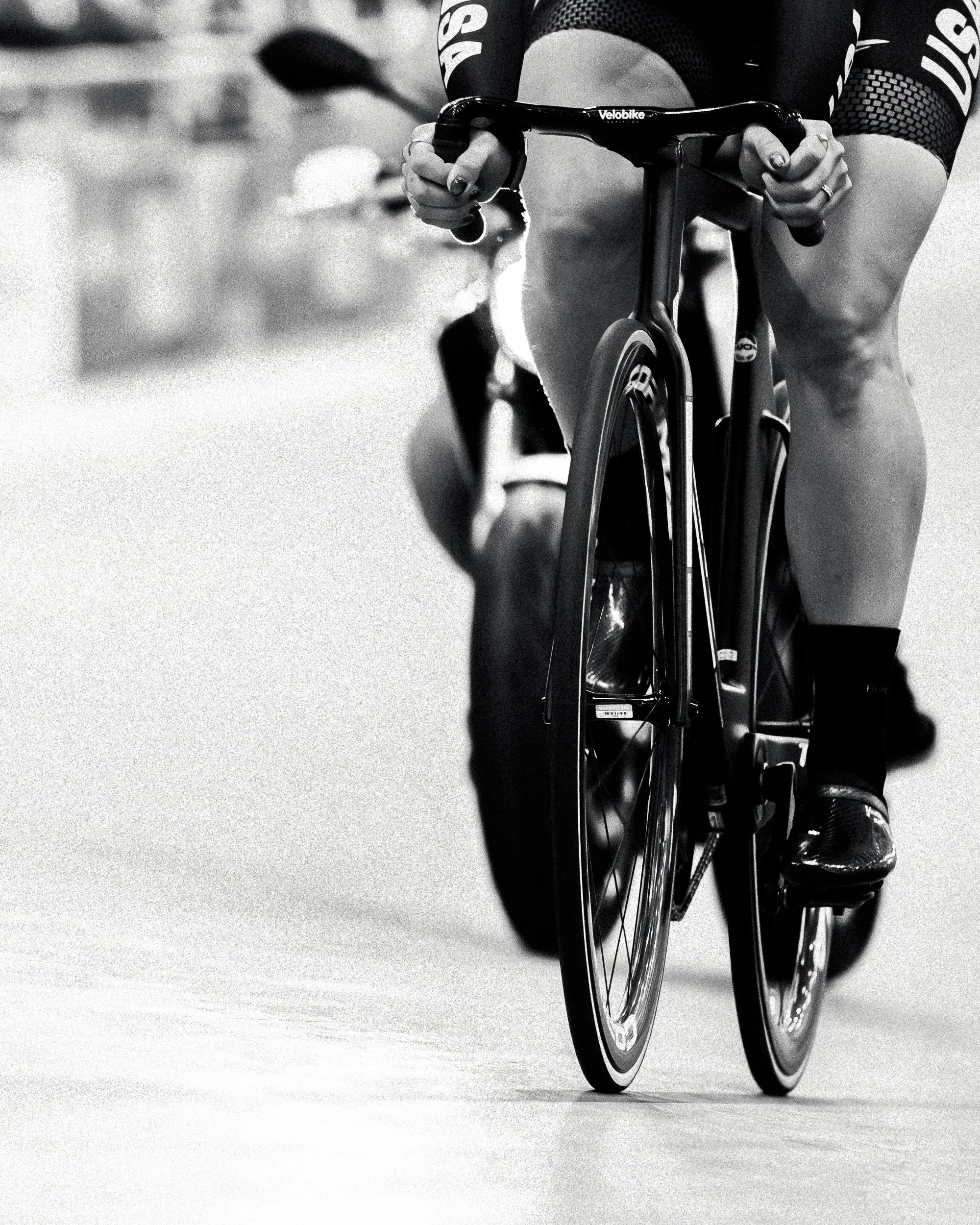 Close-up of a cyclist riding a road bike, focusing on the rider's legs and hands, in black and white.