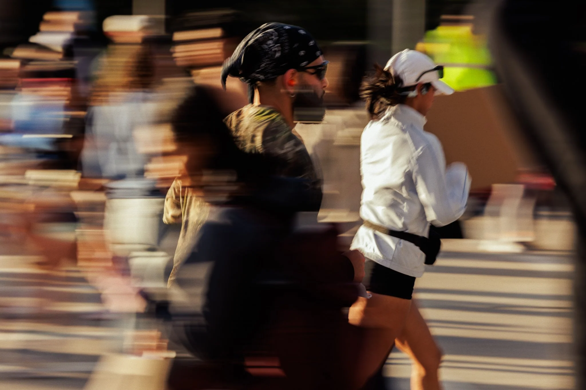 Two people running outdoors, with a blurred background of other runners and urban scenery.