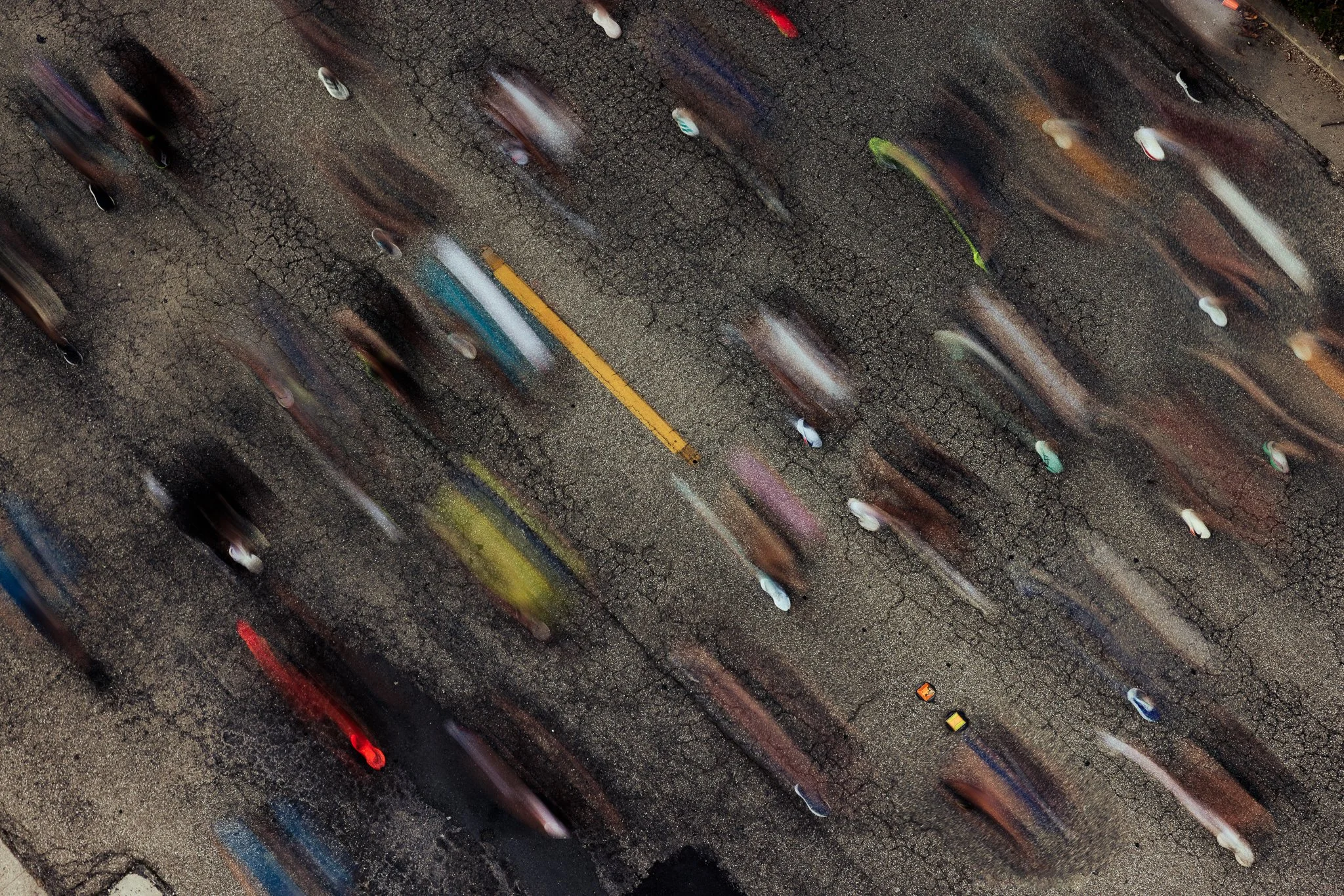 Aerial view of a busy road with blurred cars moving in different directions, seen on a rainy day with wet cracked asphalt.