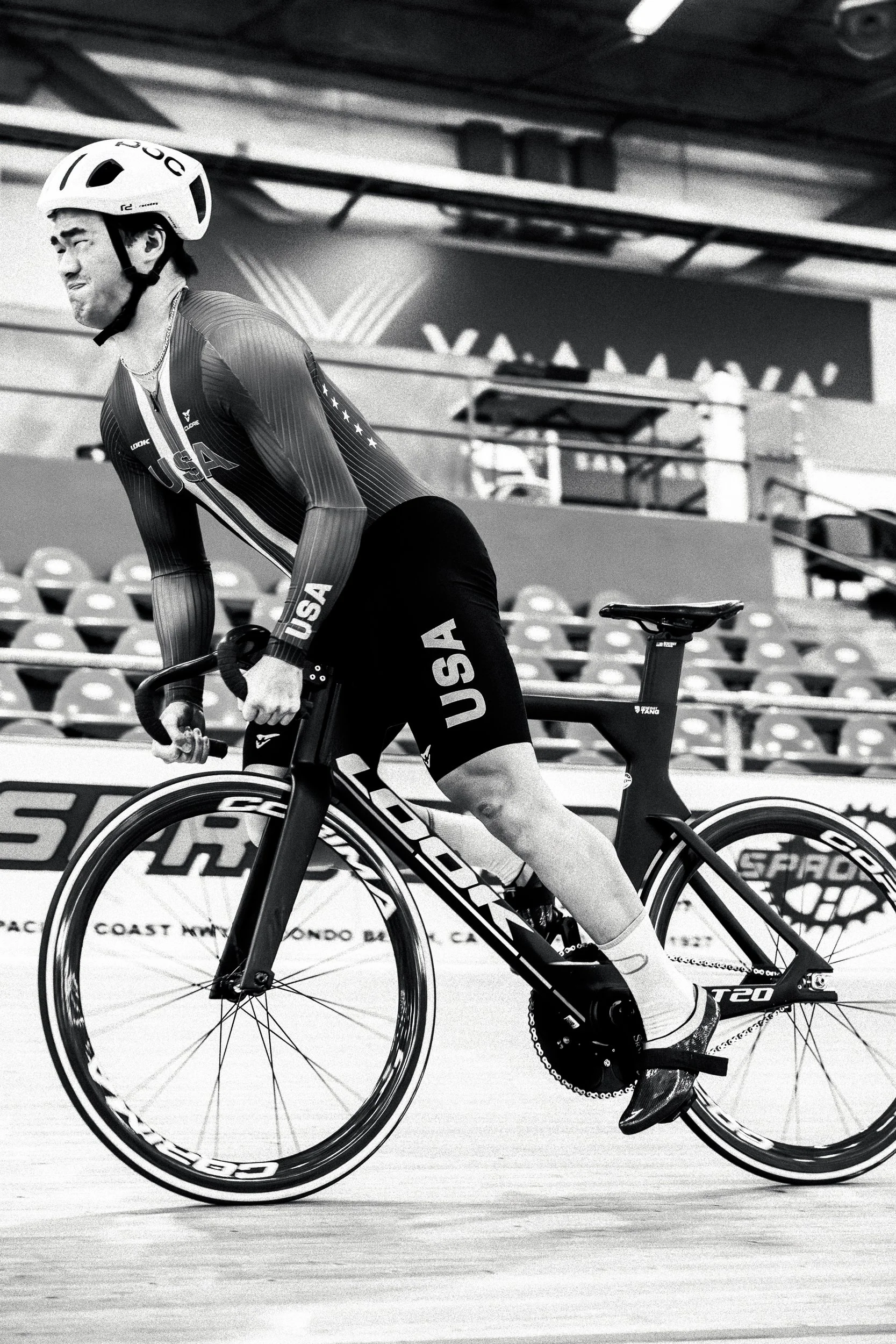 A male cyclist in USA team uniform riding a bike on an indoor velodrome track, wearing a helmet and sports gear.