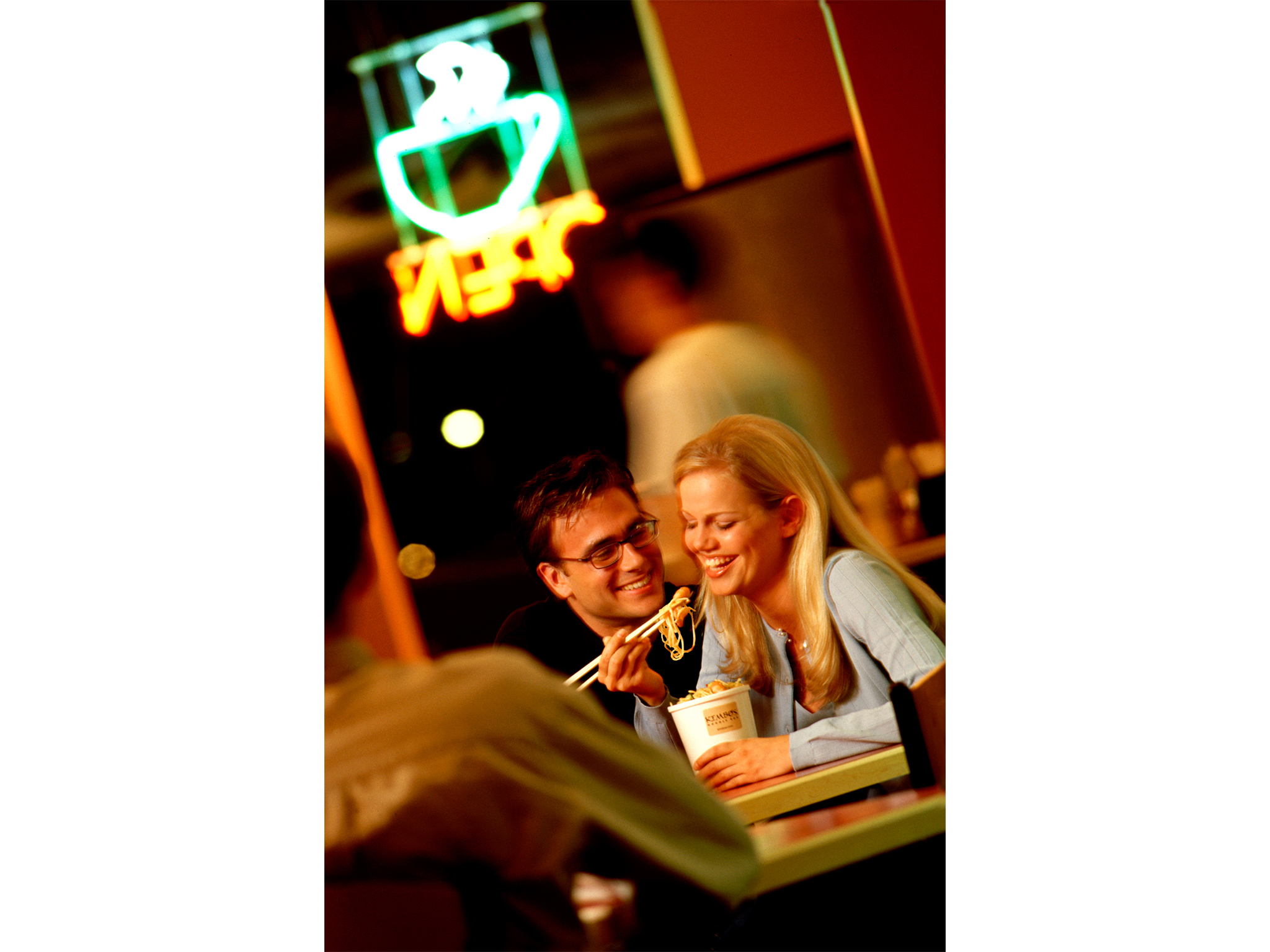 Couple eating noodles with neon sign