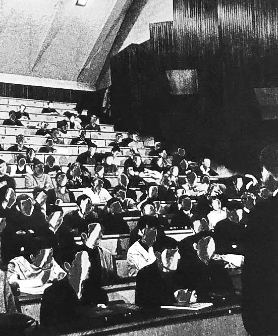 Black and white image of students in a tiered college classroom, faces are illegible