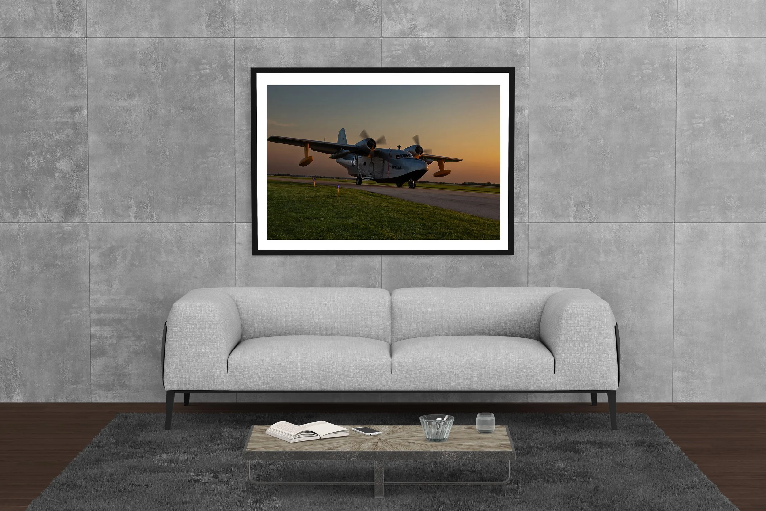 A neutral colored, modern room with a framed picture of a WWII sea plane at sunset.