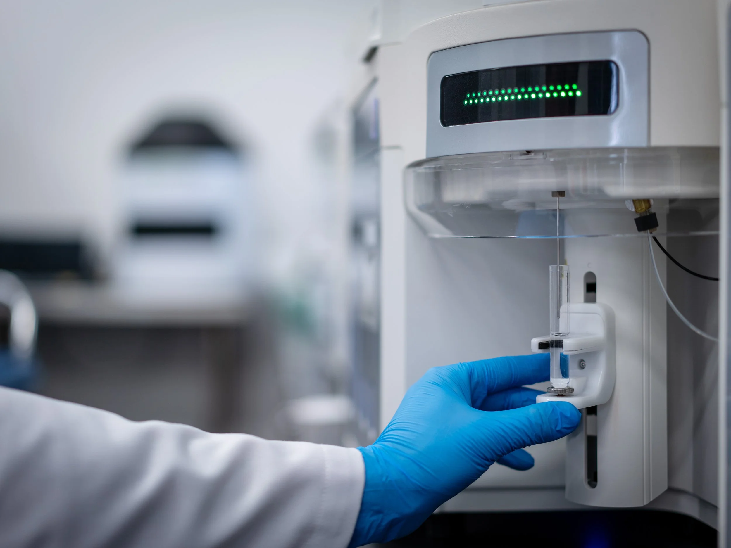 blue gloved hand places vial with water into flow cytometry machine for dental water test