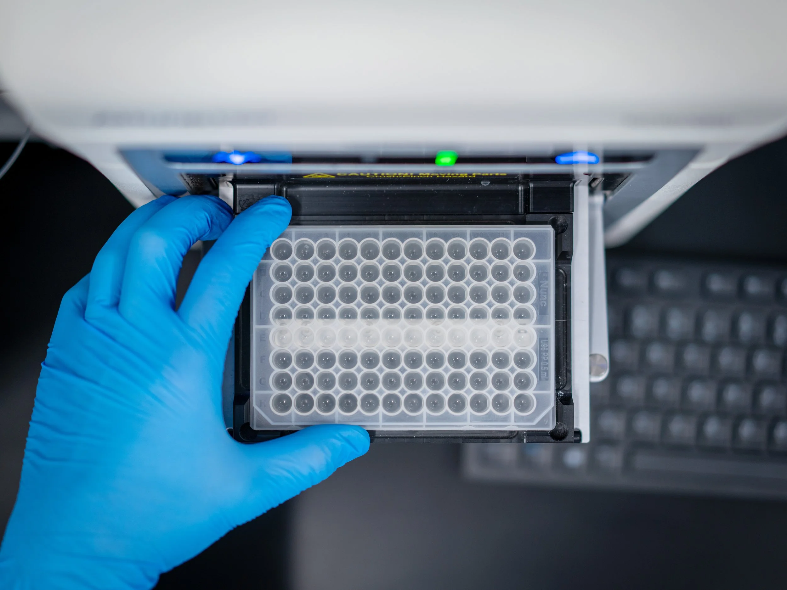 Blue gloved hand places plate of dental water samples into flow cytometry machine for reading