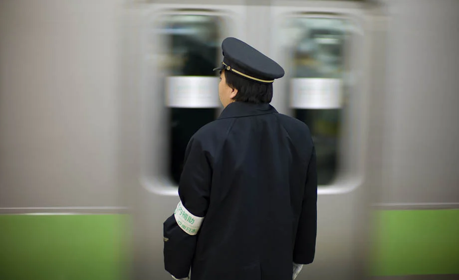 A conductor waits as a Yamanote Train passes at Shibuya Station