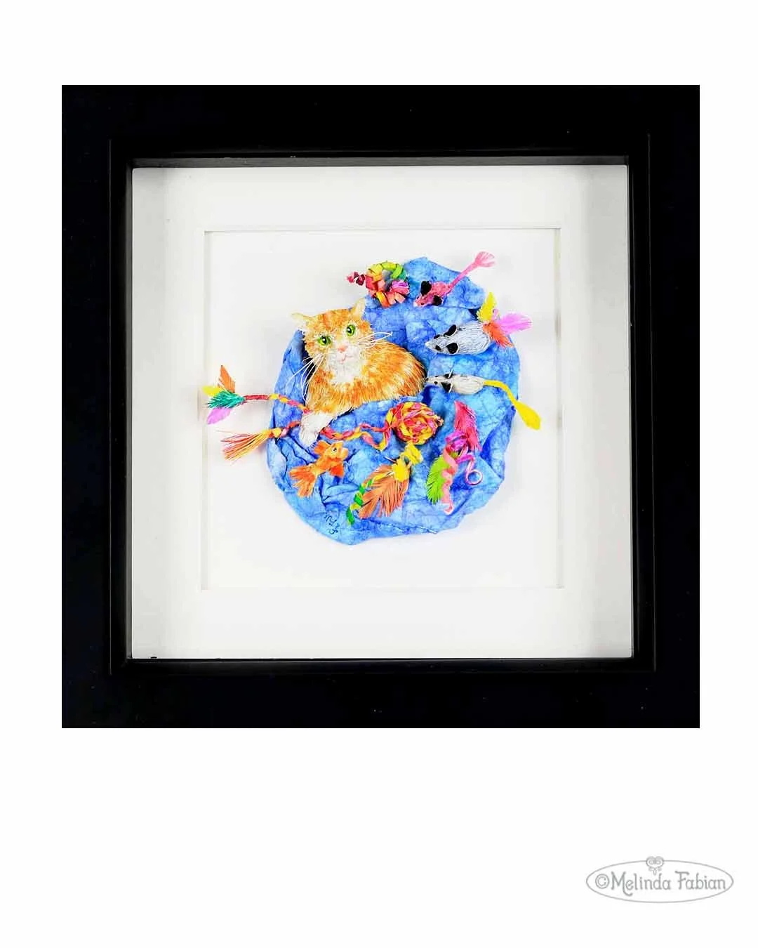 Paper Sculpture of an orange cat surrounded by a blue blanket and an organzied supply of his the cat's toys. Toy mice, fish, feathers in lots of colors. The entire sculpture is meticulously handcrafted from paper and paint. 6" x 6" x 1.25" framed art
