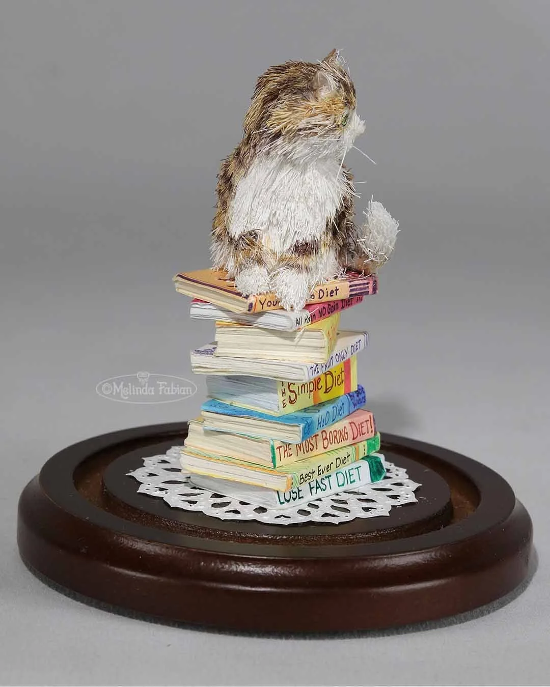 Another view of the striped cat setting on top of a stack of diet books. It is made from hand-cut paper and paint.