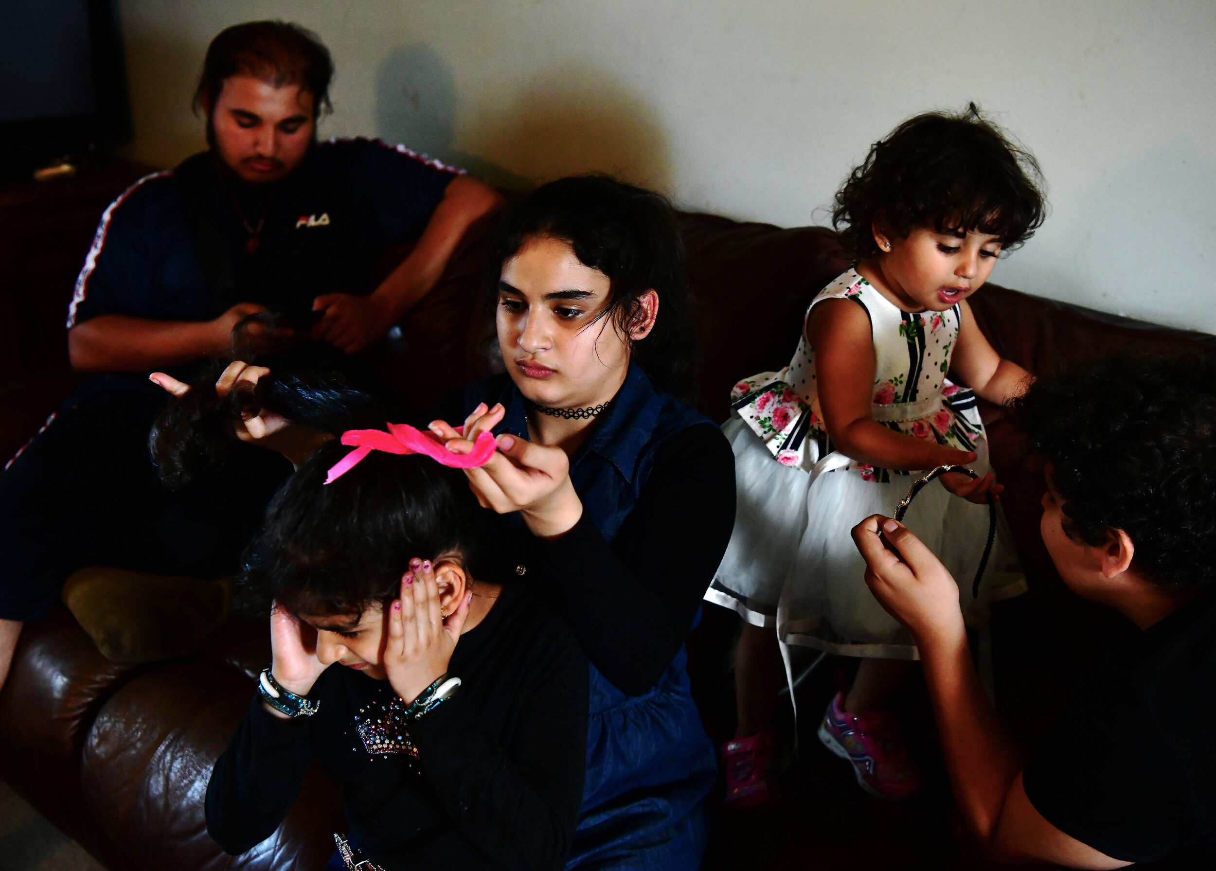  Narjes Al Hraishawi, 14, ties her younger sister’s, Fatima’s, hair Asinat, right, 2, tries to grab her headband from her older brother, Ali, 12. Abbas, left, 17, watches Youtube videos before driving two of the children to a carnival on Friday, Augu