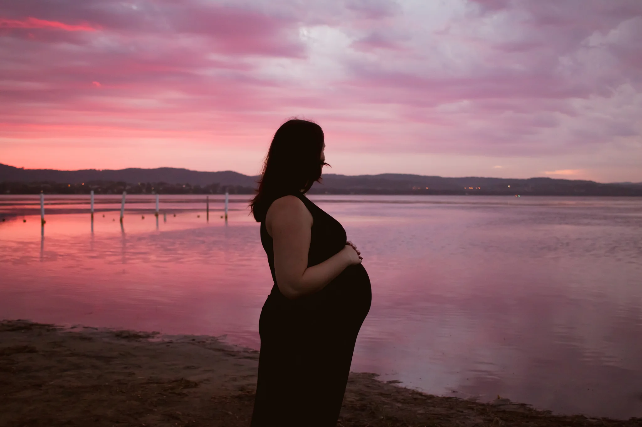 pink and red sunset at long jetty with pregnant woman
