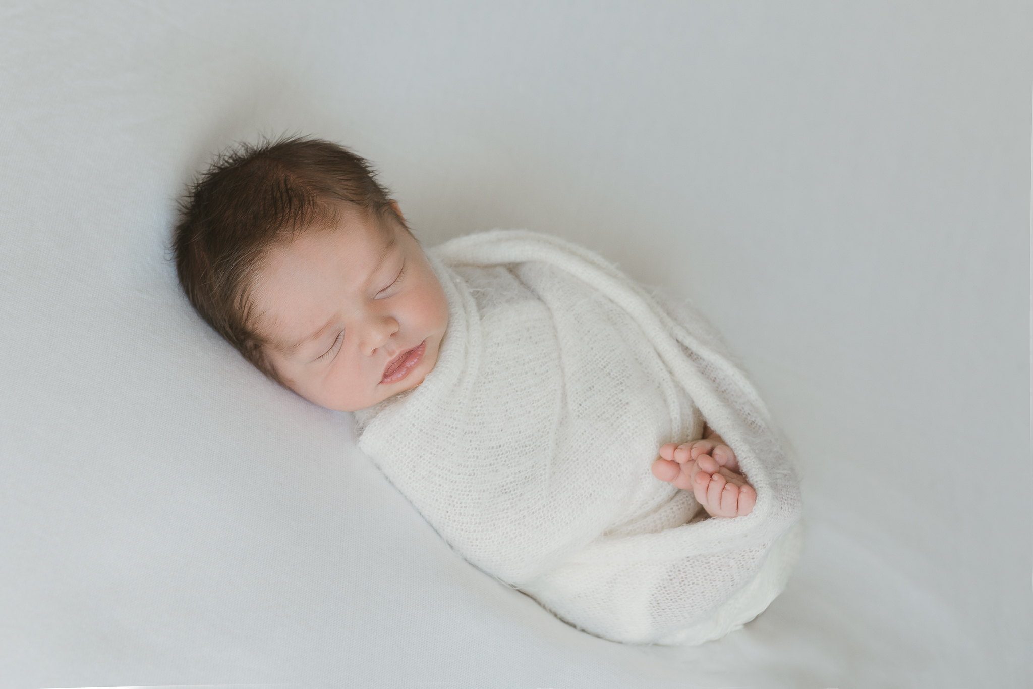 baby wrapped in white on natural white background