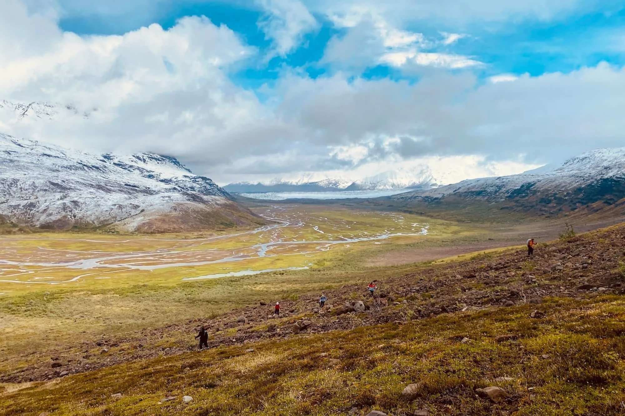 Hikers hiking up a hill with snow capped mountains behind.