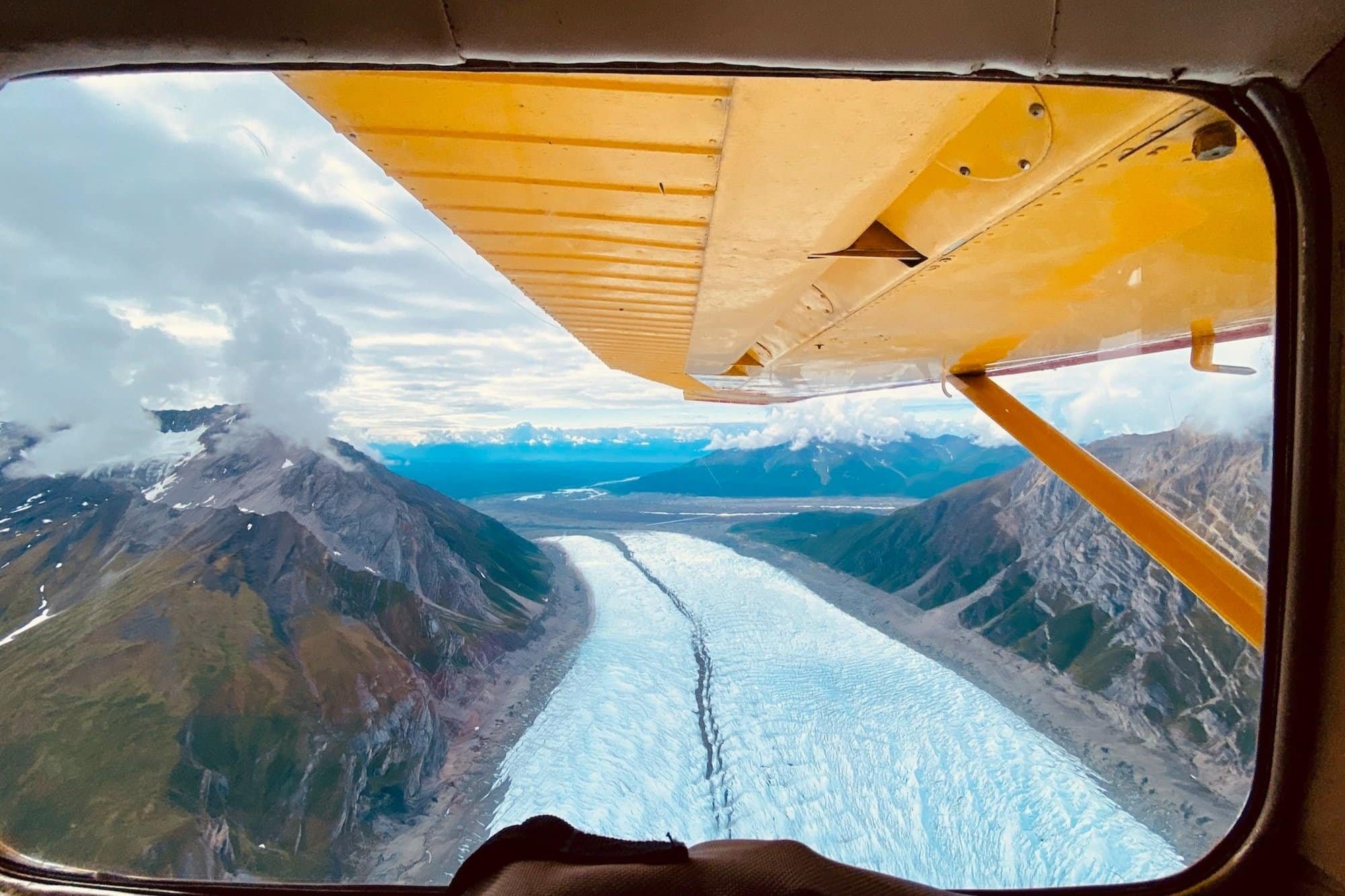 Looking out of bush plane window at bright white glacier below.