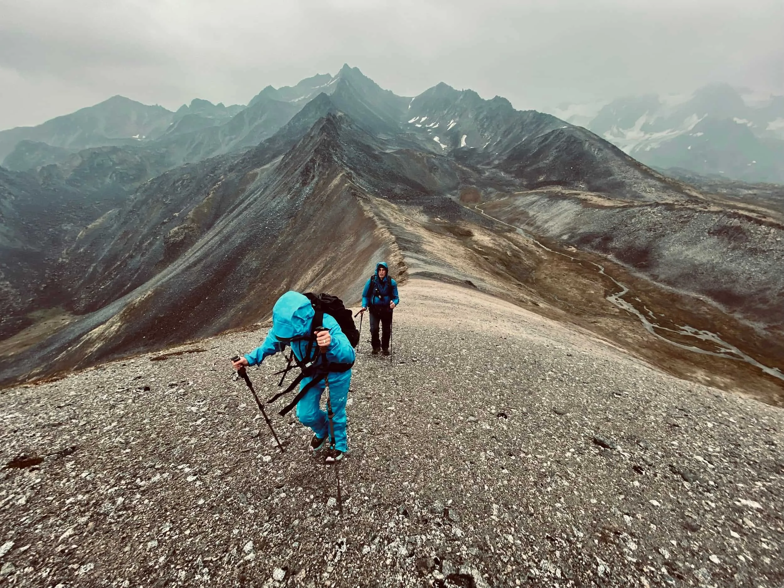 Two backpackers walking up a ridge in a rain storm.
