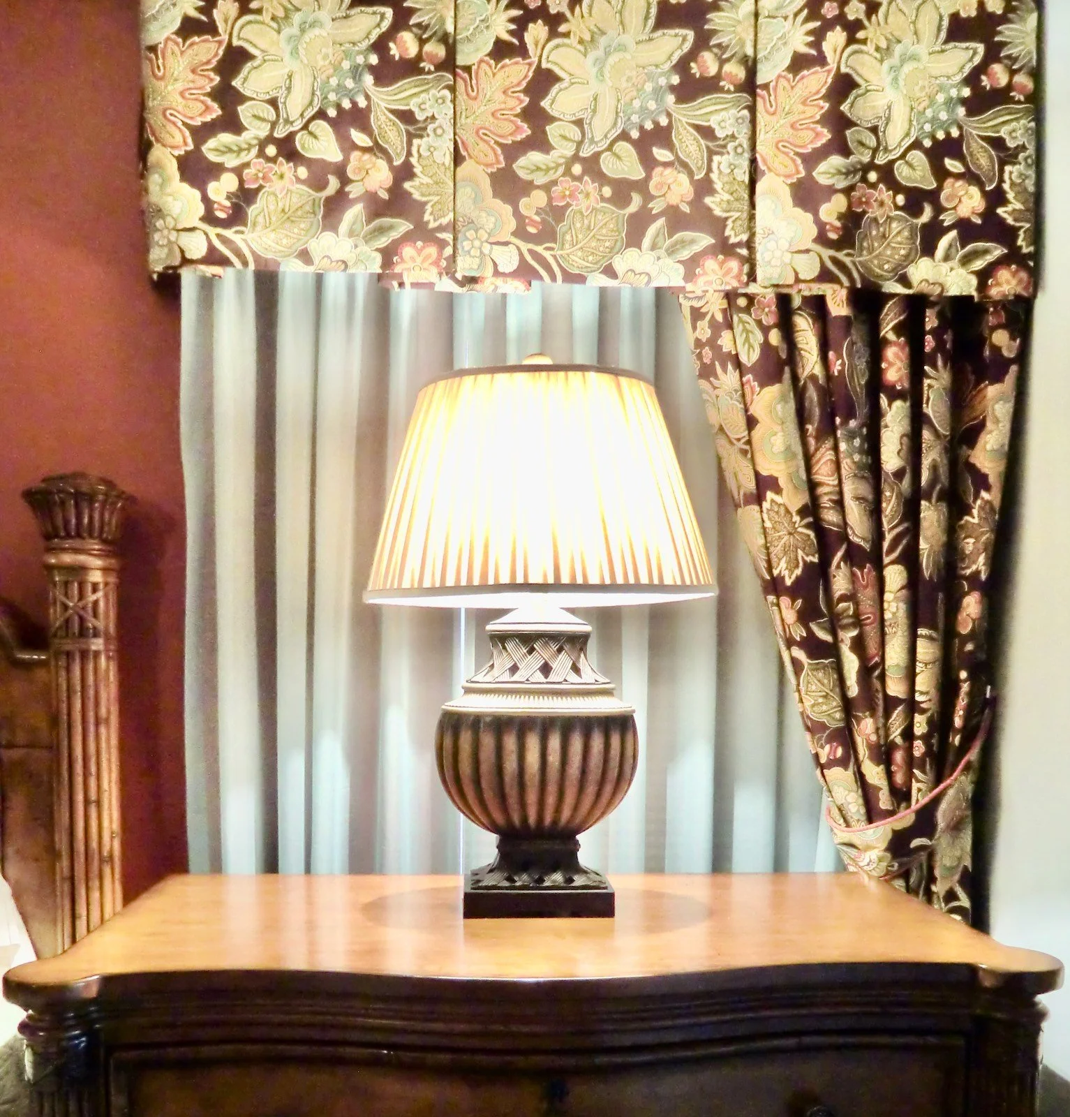 Luxury coastal bedroom with dark Tommy Bahamas nightstand with lamp in front of tropical drapery