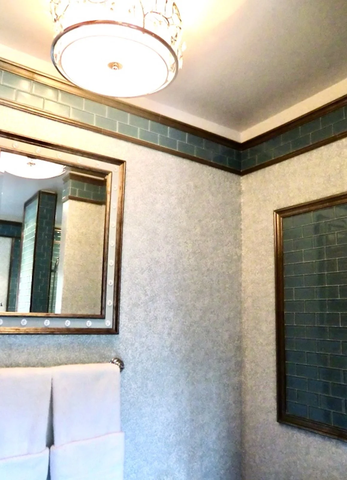 coastal style bathroom with blue glass tiles and silver trim as a ceiling detail and wall panel over toilet