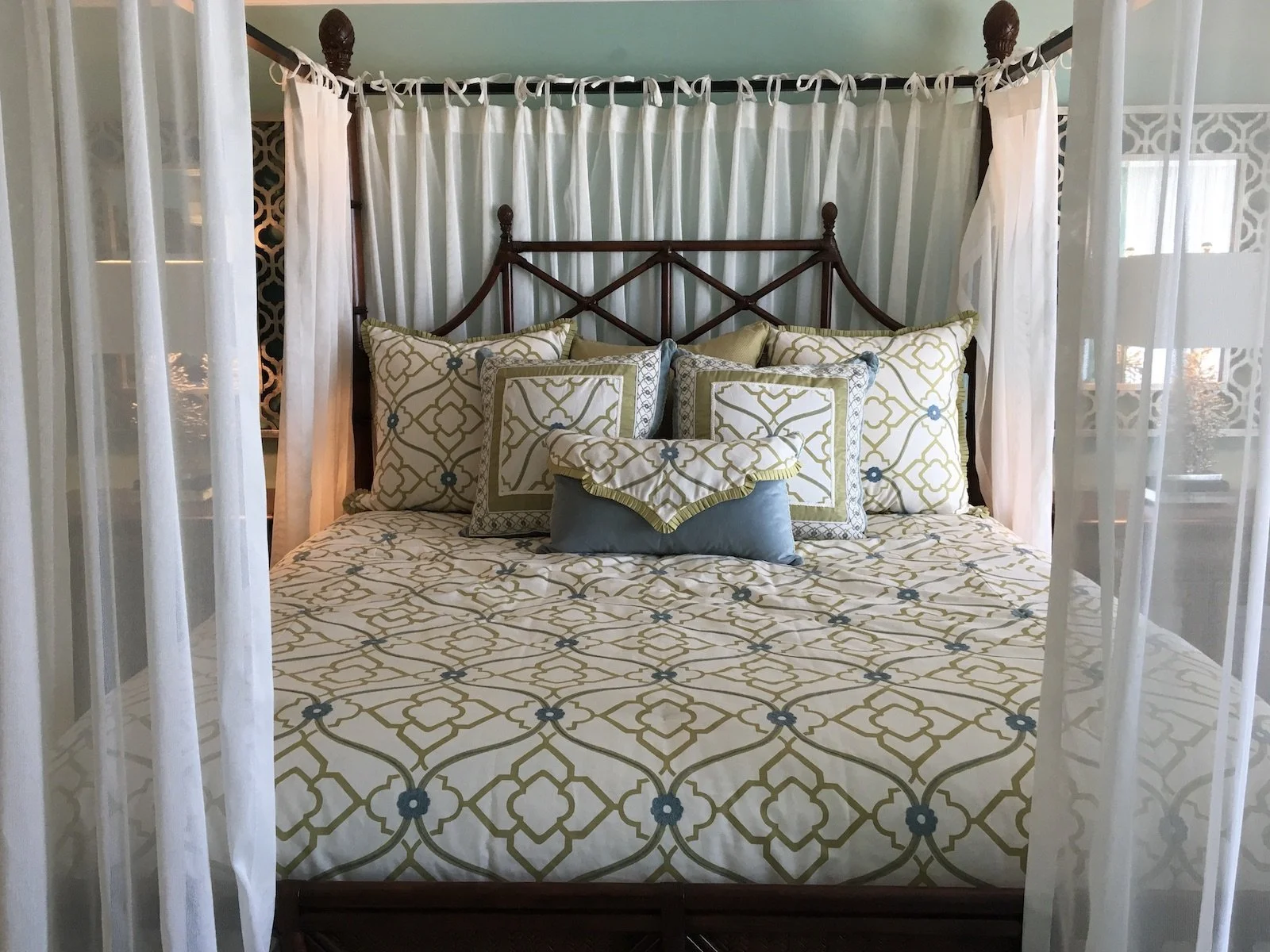 Modern British Colonial four poster bed with dark bamboo and Ratan with custom bedding and white sheer curtains at Ocean Reef Club