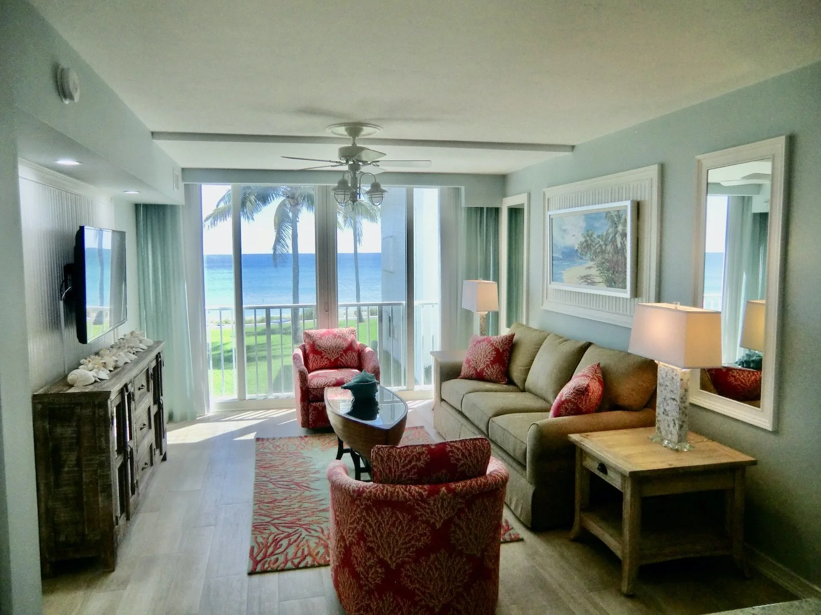 Modern coastal living room with aqua walls, tan sofa, two coral chairs, and driftwood console at Ocean Reef Club