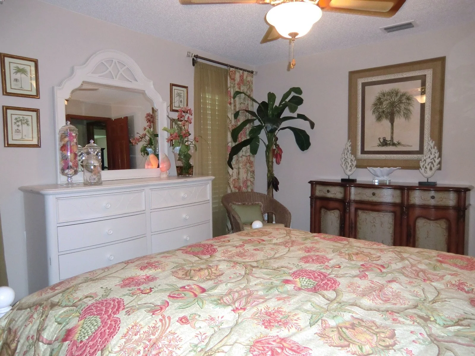 coastal style bedroom with tropical bedspread, white furniture and antique credenza in Palm Beach