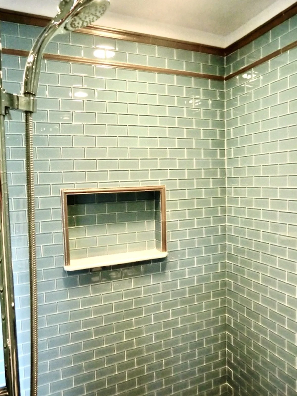 walk in shower with niche made with aqua glass tiles and silver trim
