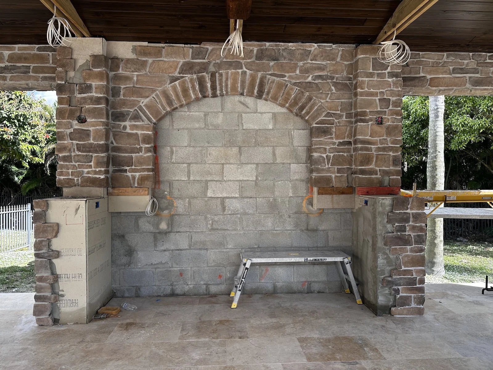 pool pavilion under construction with bar having stone columns, arch, and tile mural
