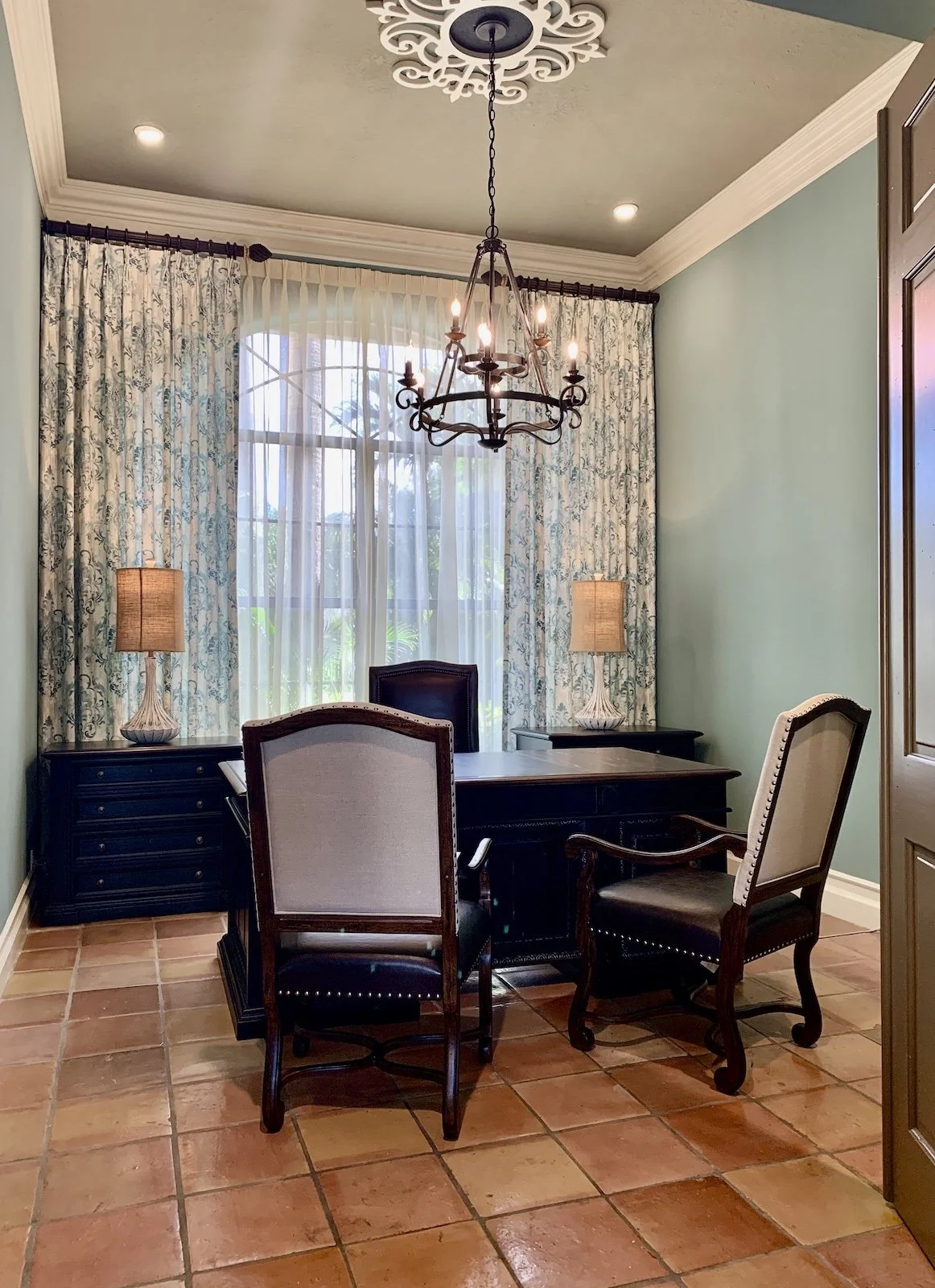 Mediterranean home office with a traditional dark wood desk with chairs and matching file cabinets flanking wall of custom drapery