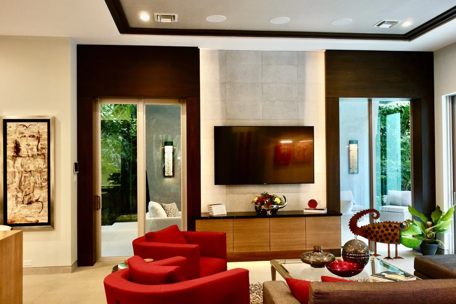 Modern family room with architectural stone TV wall and dark wood surround at flanking doors in Las Olas custom home