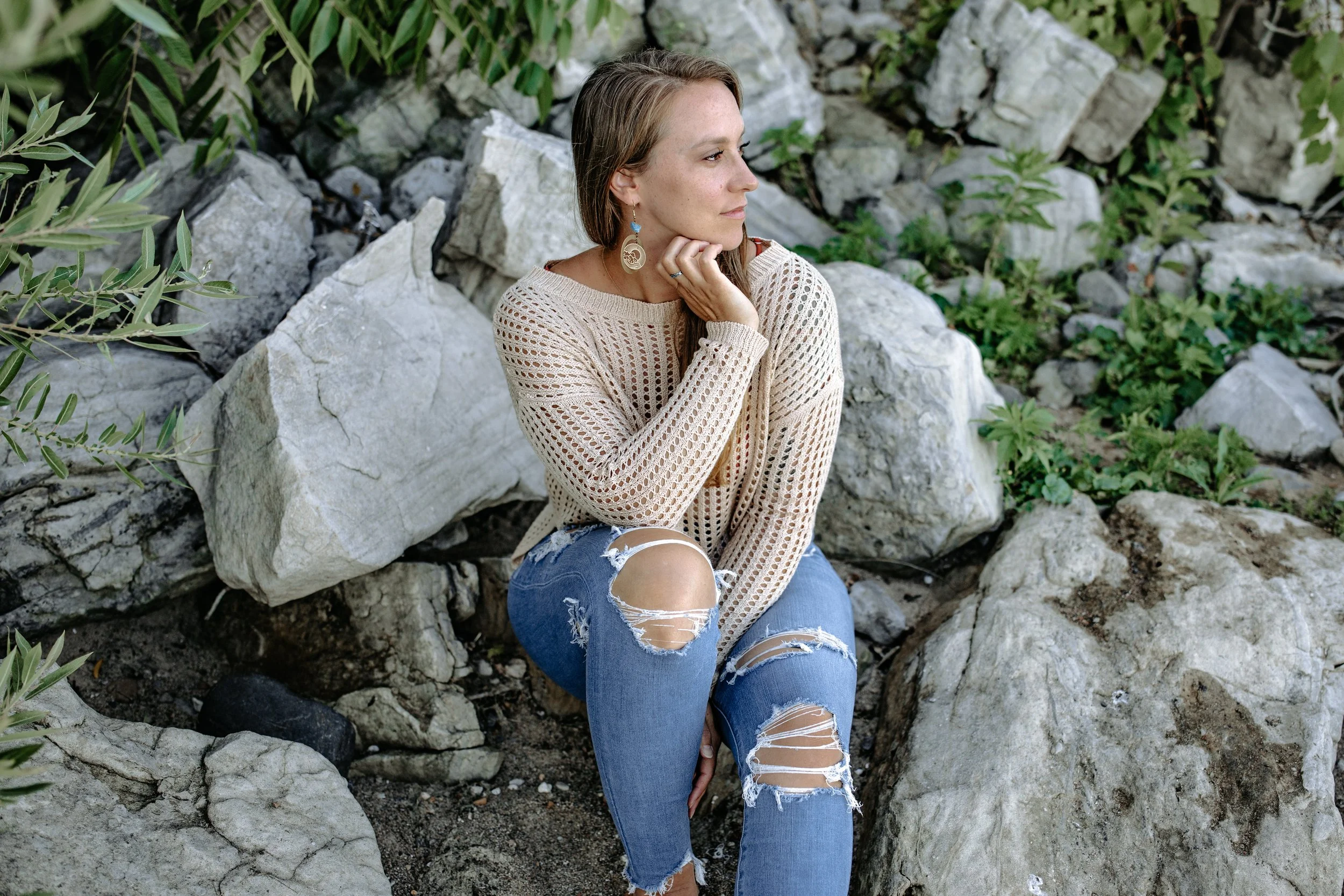 Wendy sits on a rocky hill surrounded by greenery looking off into the distance thinking about photography.