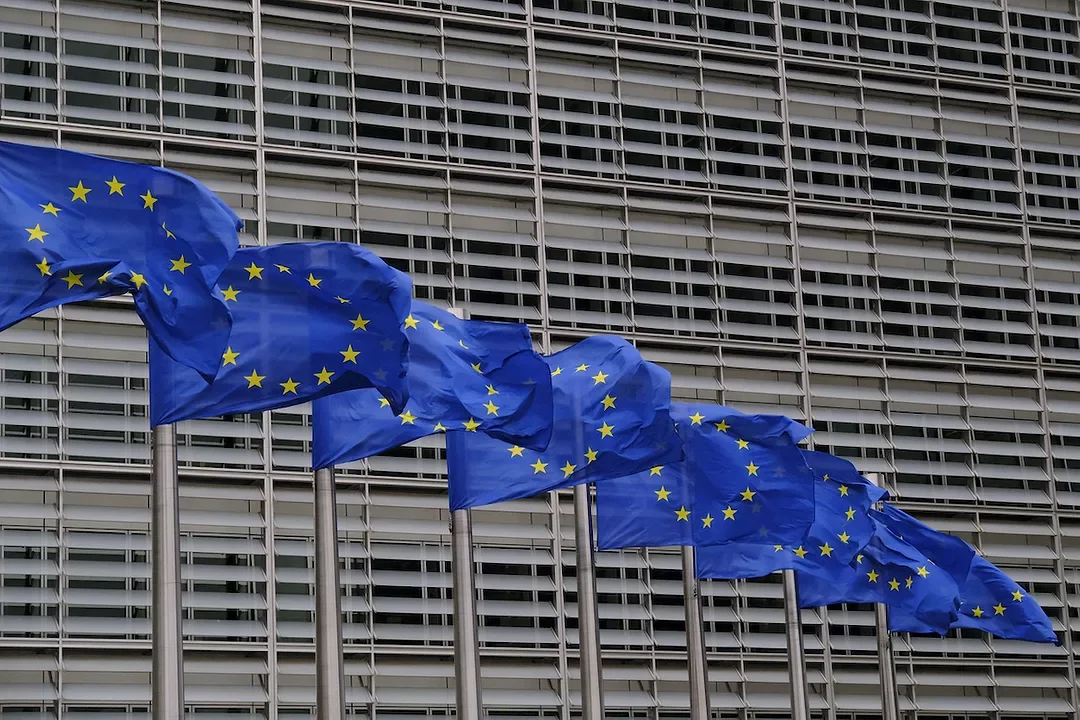 a row of European Union flags flying in a breeze in front of a building with metal outer shell