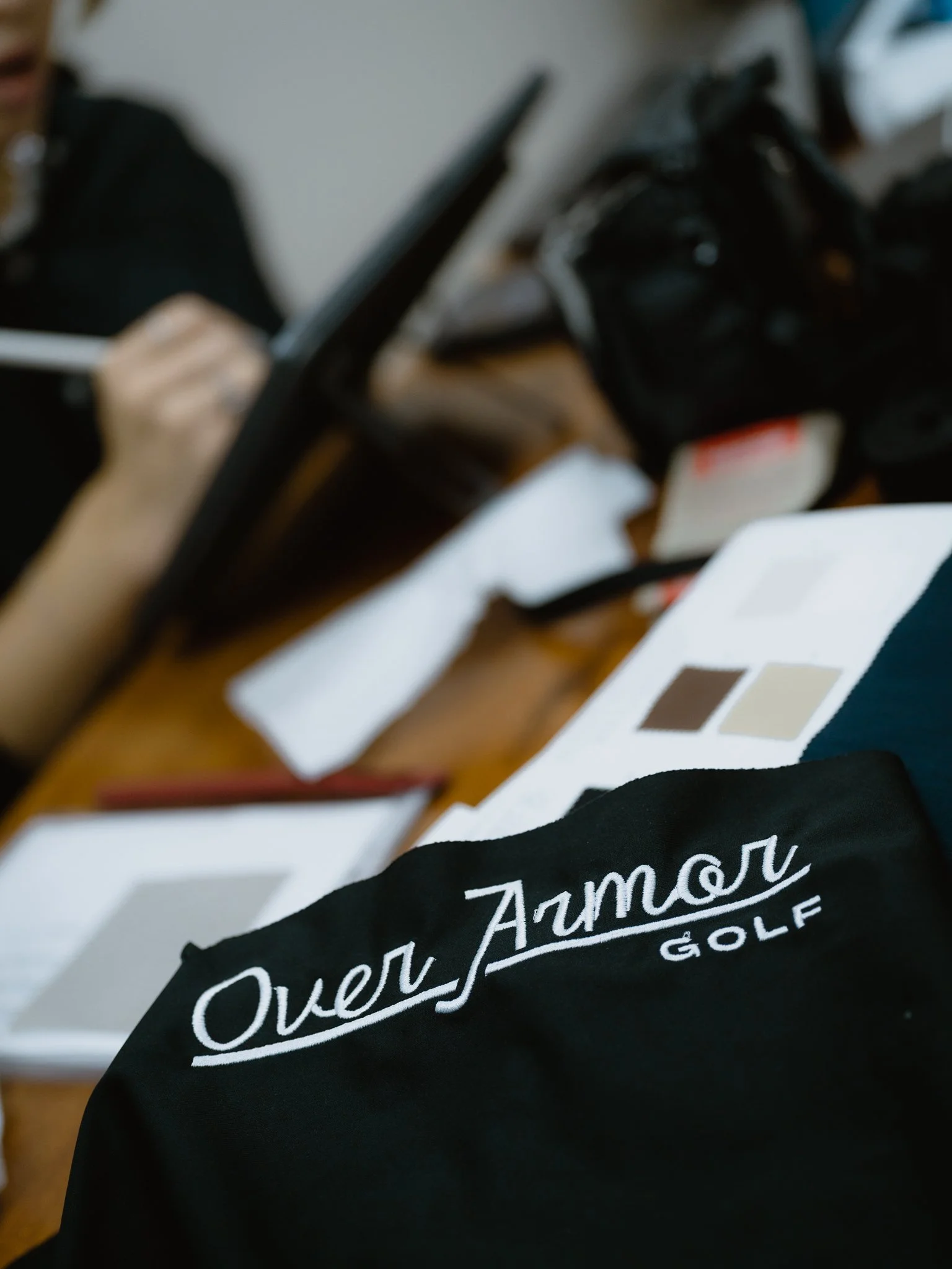 embroidered logo of Over Armor Golf on the factories designer's workplace for quality check