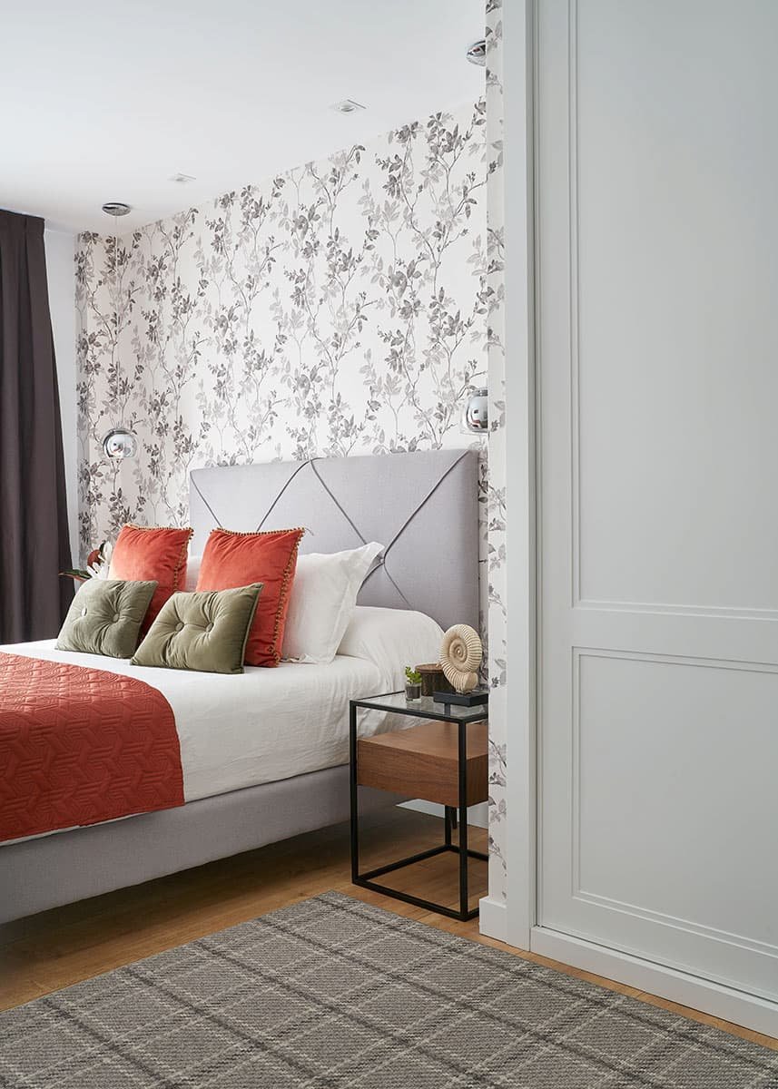 Detalle de dormitorio con cabecero tapizado y mesilla auxiliar en vivienda en Urduliz Bizkaia con papel pintado floral proyecto de interiorismo y estilismo.