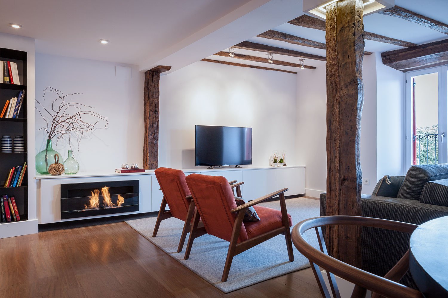 Salón moderno con chimenea y vigas de madera en vivienda reformada en Bizkaia con zona de estar mobiliario de estilo contemporáneo proyecto de interiorismo.