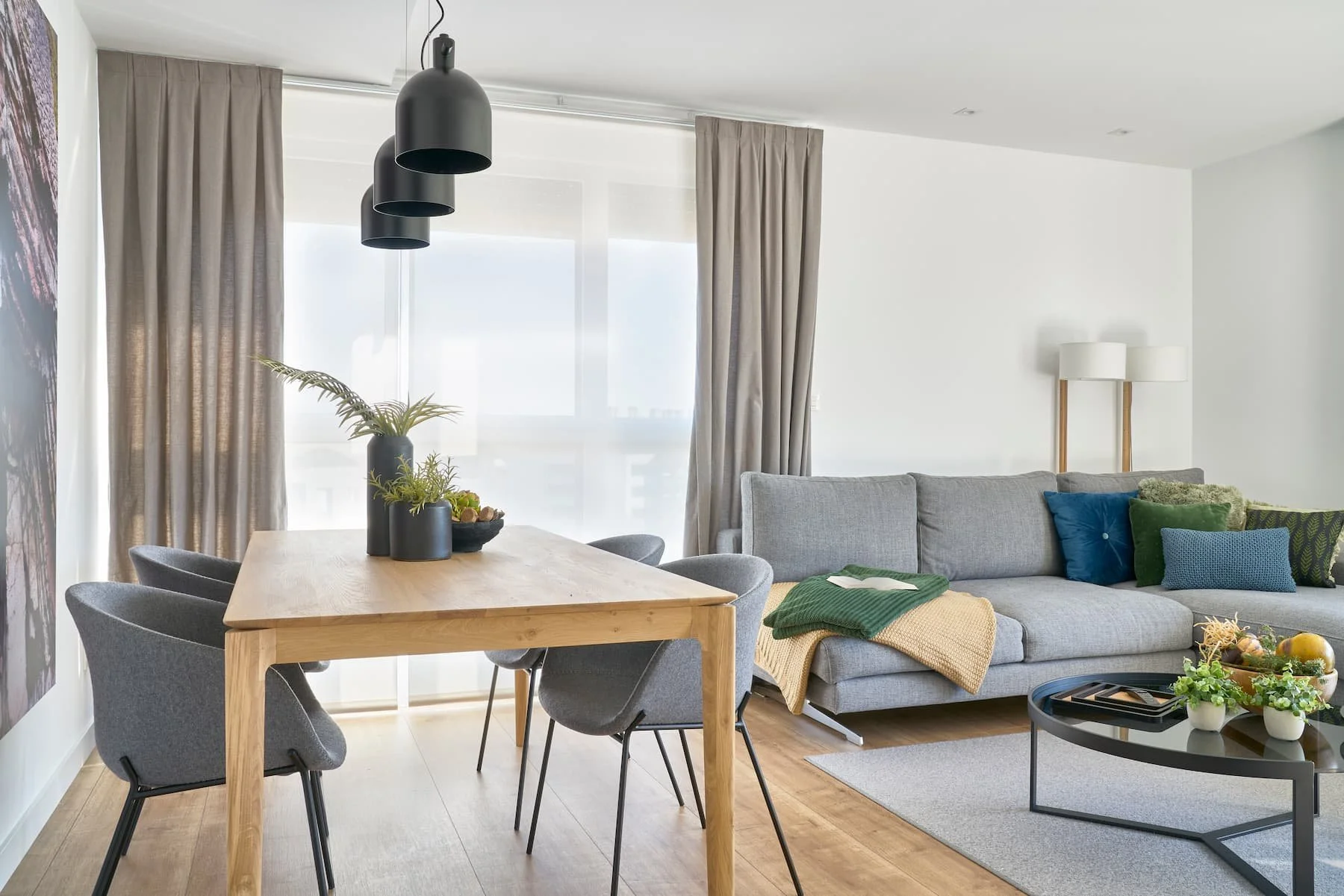 Salón comedor moderno con sofá gris, mesa de madera y lámparas colgantes en protecto de decoración y estilismo en Urduliz