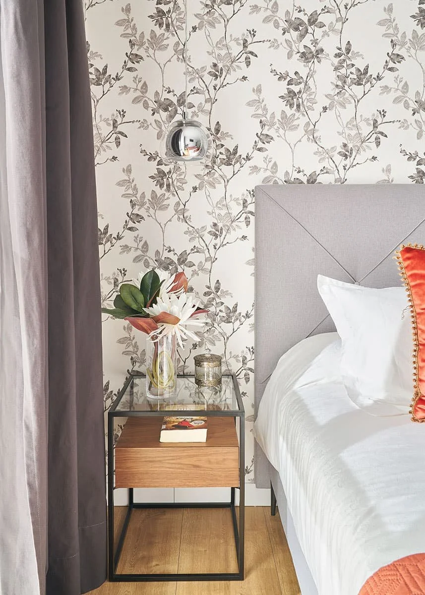Mesilla de noche con decoración, jarrón de cristal con flores junto a cabecero tapizado en tela gris en dormitorio en vivienda en Urduliz Bizkaia proyecto de interiorismo y estilismo.