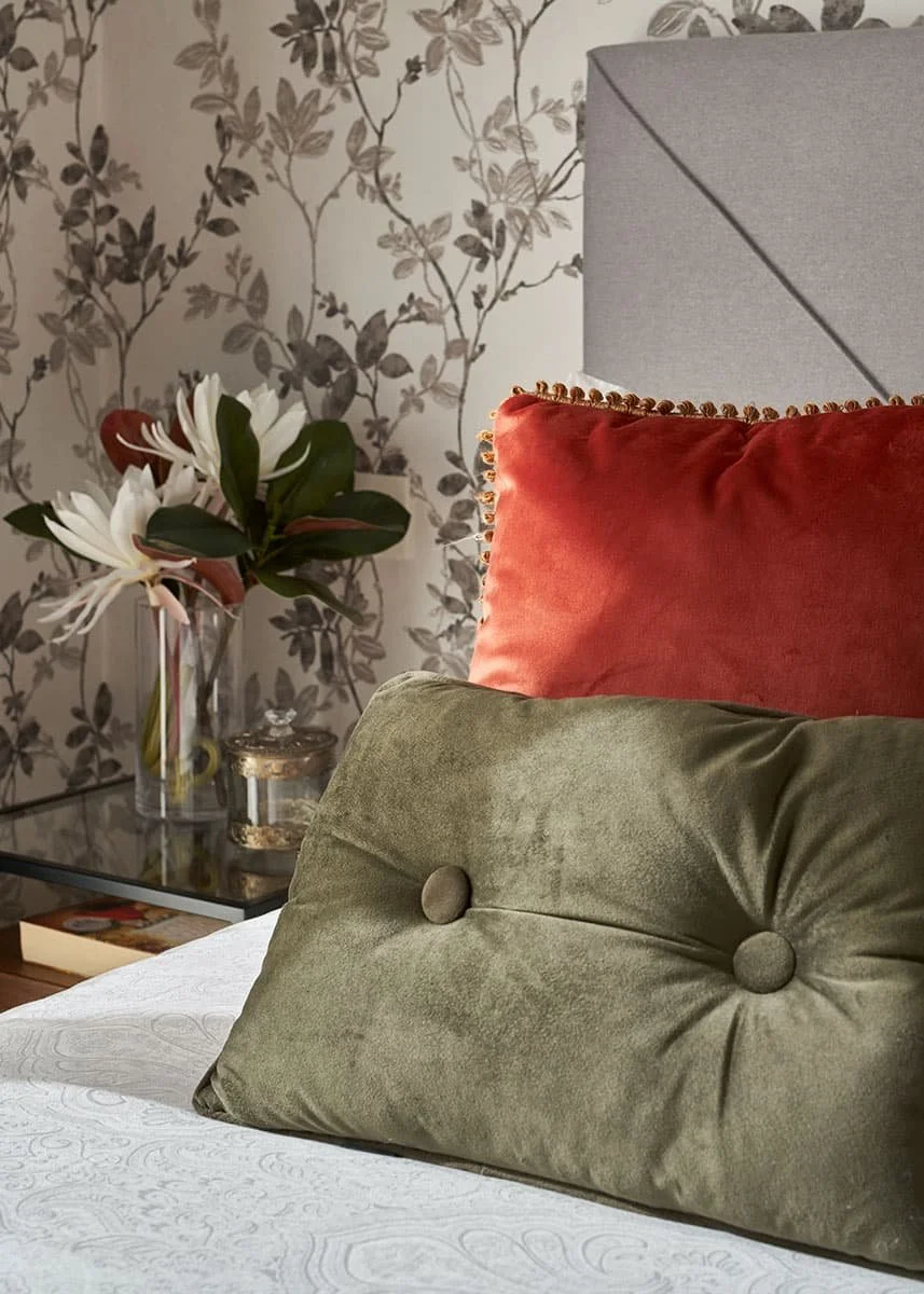 Detalle de cojines decorativos en dormitorio con cabecero tapizado en tela gris y papel pintado con motivos florales en vivienda de Urduliz Bizkaia proyecto de interiorismo y estilismo.