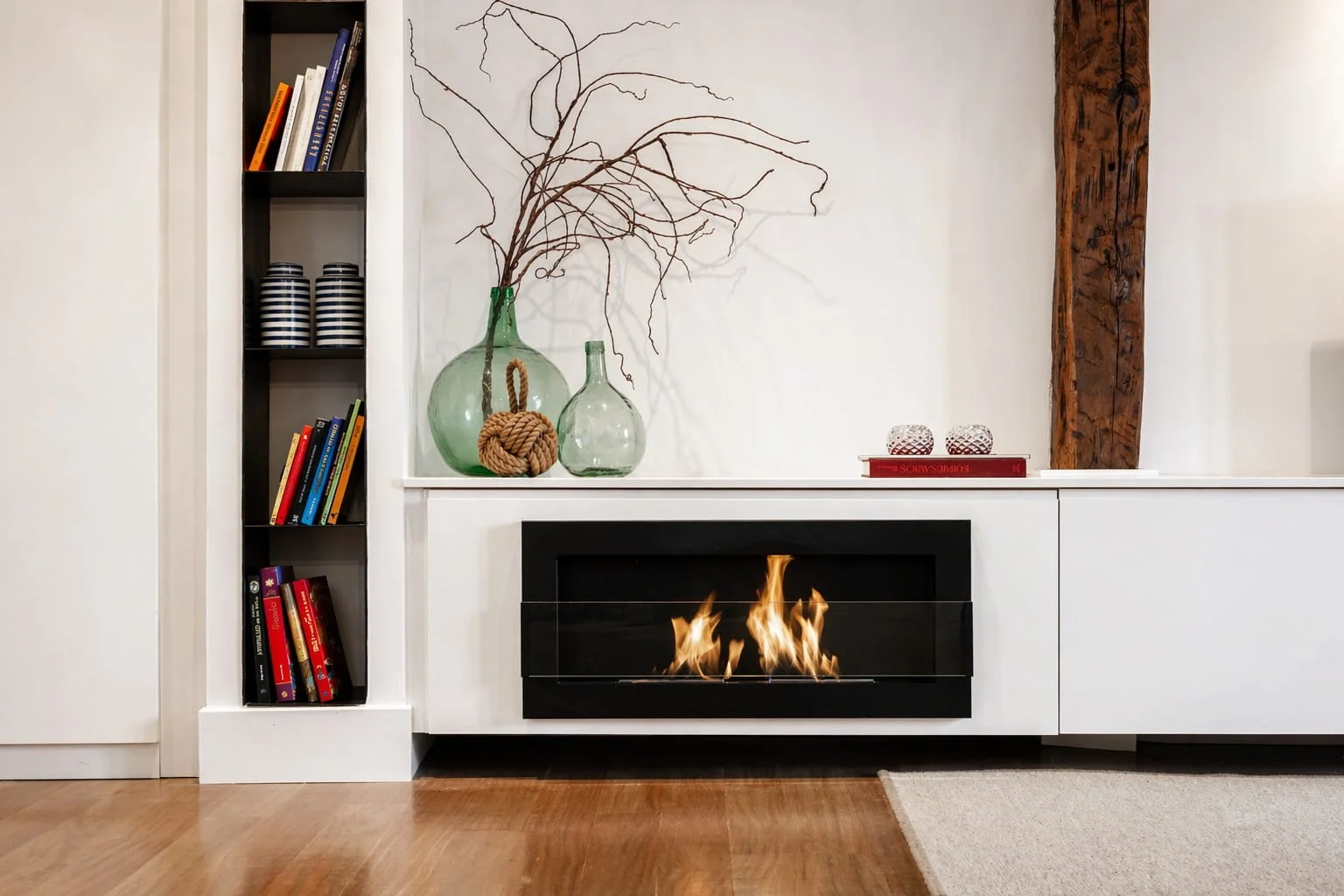 Detalle de chimenea integrada en mueble blanco con decoración en vidrio y madera en vivienda de Mundaka