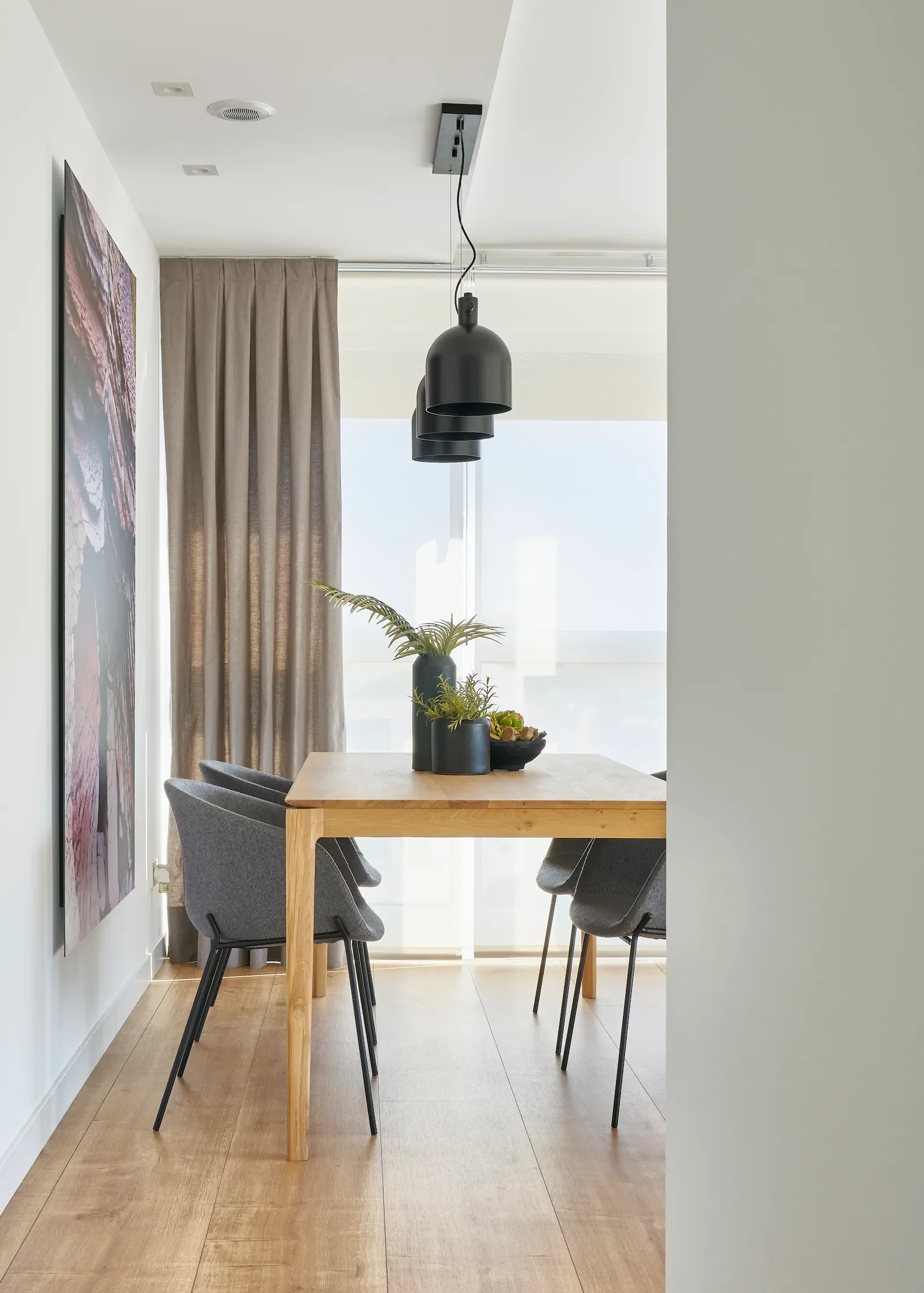 Comedor moderno con mesa de madera, sillas tapizadas oscuras y lámpara colgante en vivienda en Urduliz