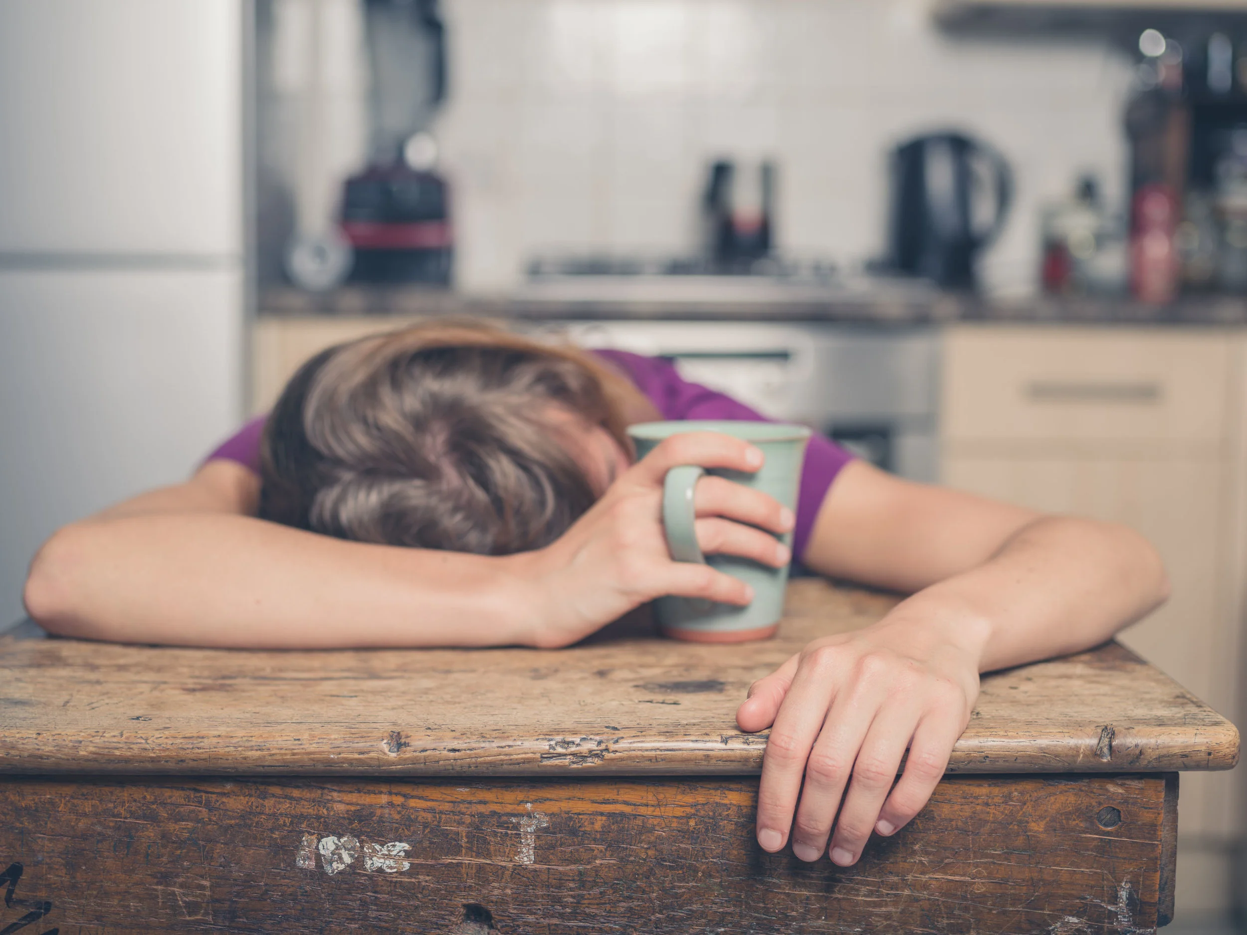 43388665 - a tired young woman is having a cup of tea and is resting her head on a table