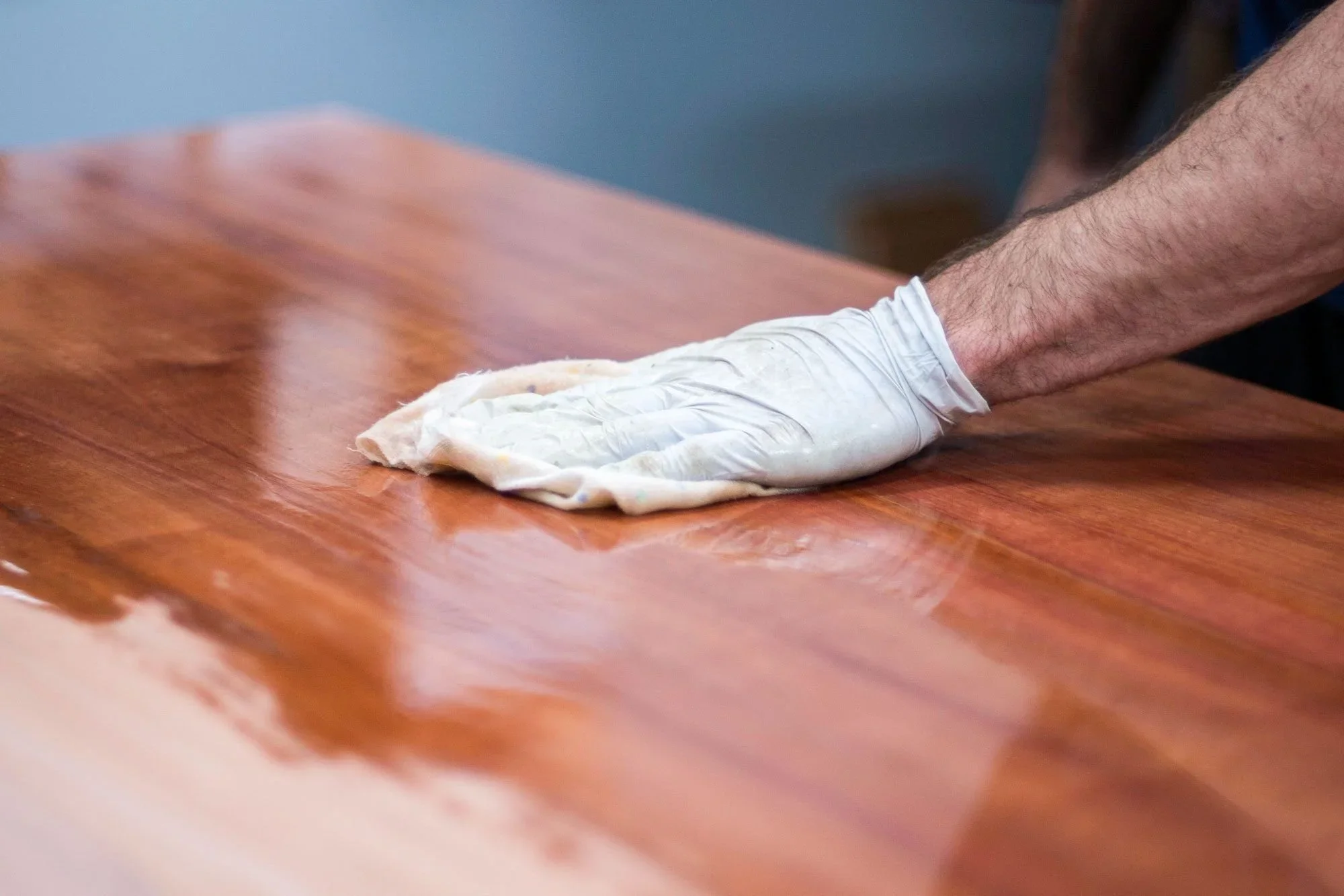 Person applying wood wax and polish to wooden furniture surface with cloth and glove